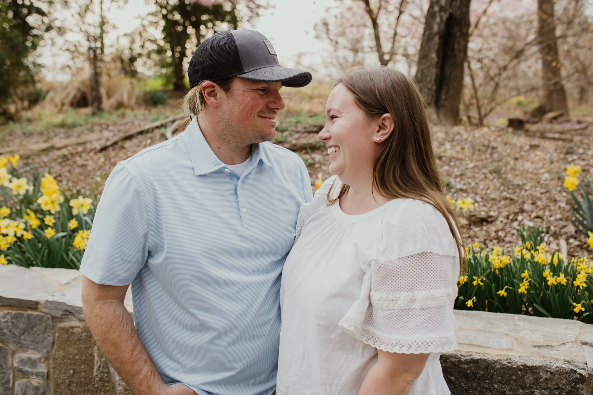 Smiling engaged couple during a spring engagement session in Northern Virginia, photographed in a relaxed, documentary style with seasonal flowers in bloom.