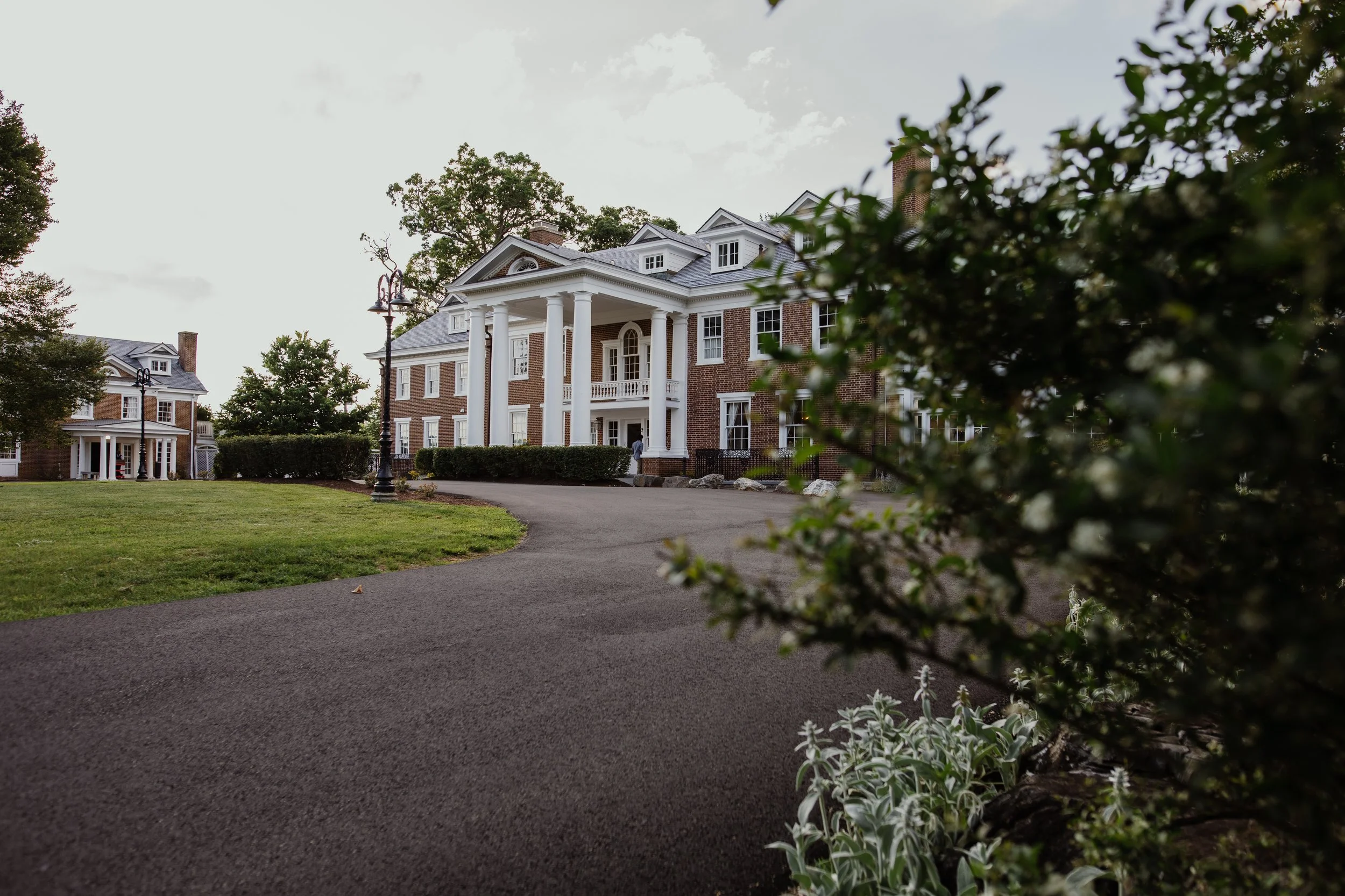 Exterior view of Raspberry Plain Manor wedding venue in Leesburg, Virginia with white columns and landscaped grounds at sunset.