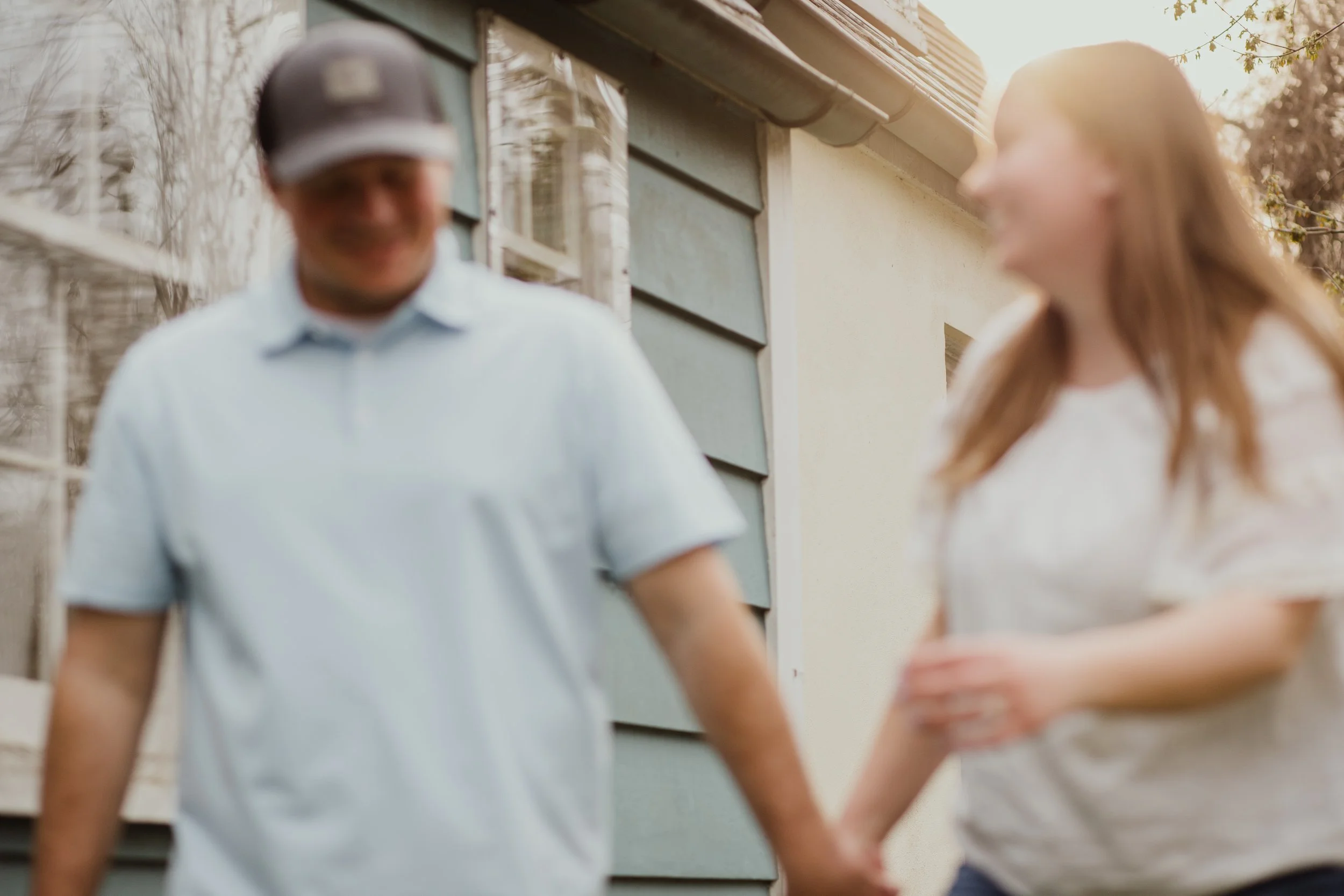 Candid engagement photo of a couple holding hands and walking outside in Northern Virginia during golden hour, photographed in a relaxed, documentary style.