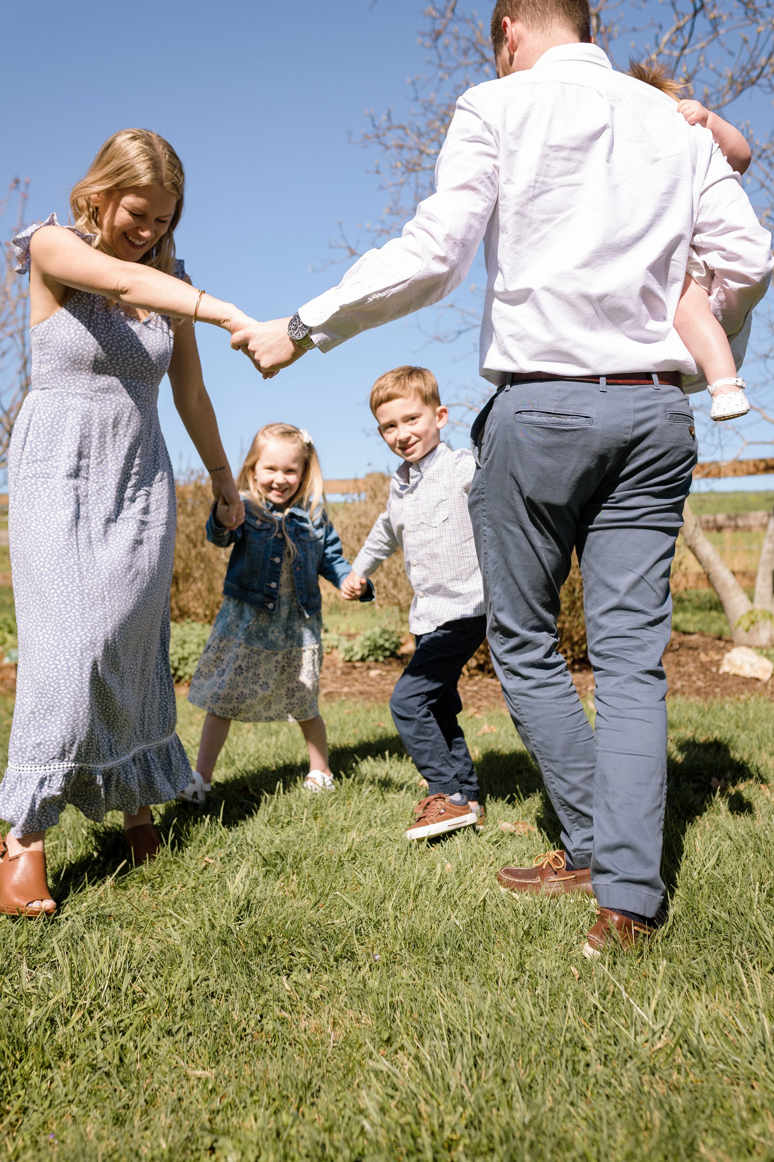 Family of five walking hand in hand through the grass during a spring morning family session at Rady Park in Fauquier County.