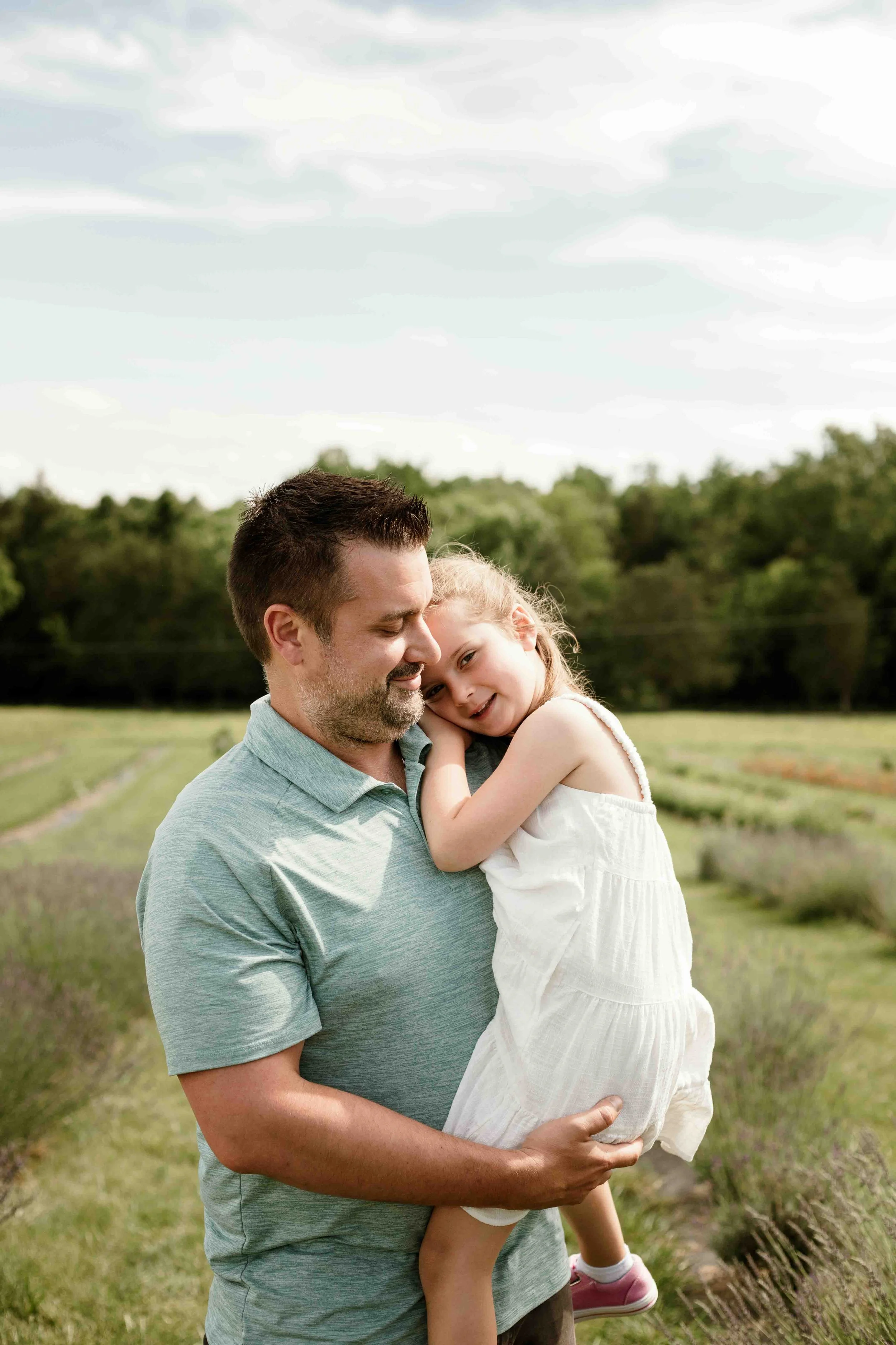 Father holding his young daughter in a lavender field during a summer family photography session at Seven Oaks Lavender Farm in Fauquier County, Virginia.