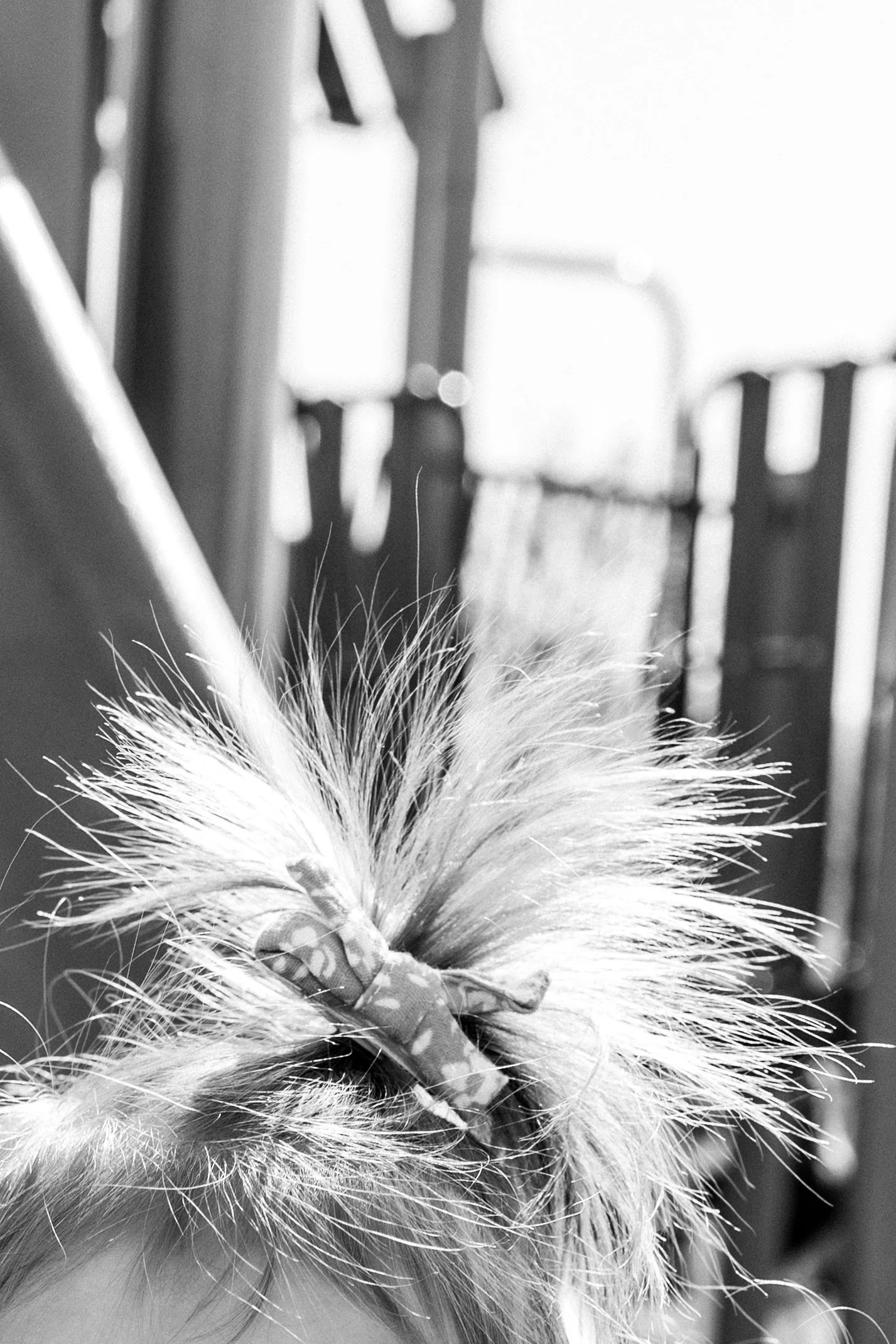 Black and white close-up detail of a toddler’s windblown hair and bow on the playground during a family session at Rady Park in Fauquier County.