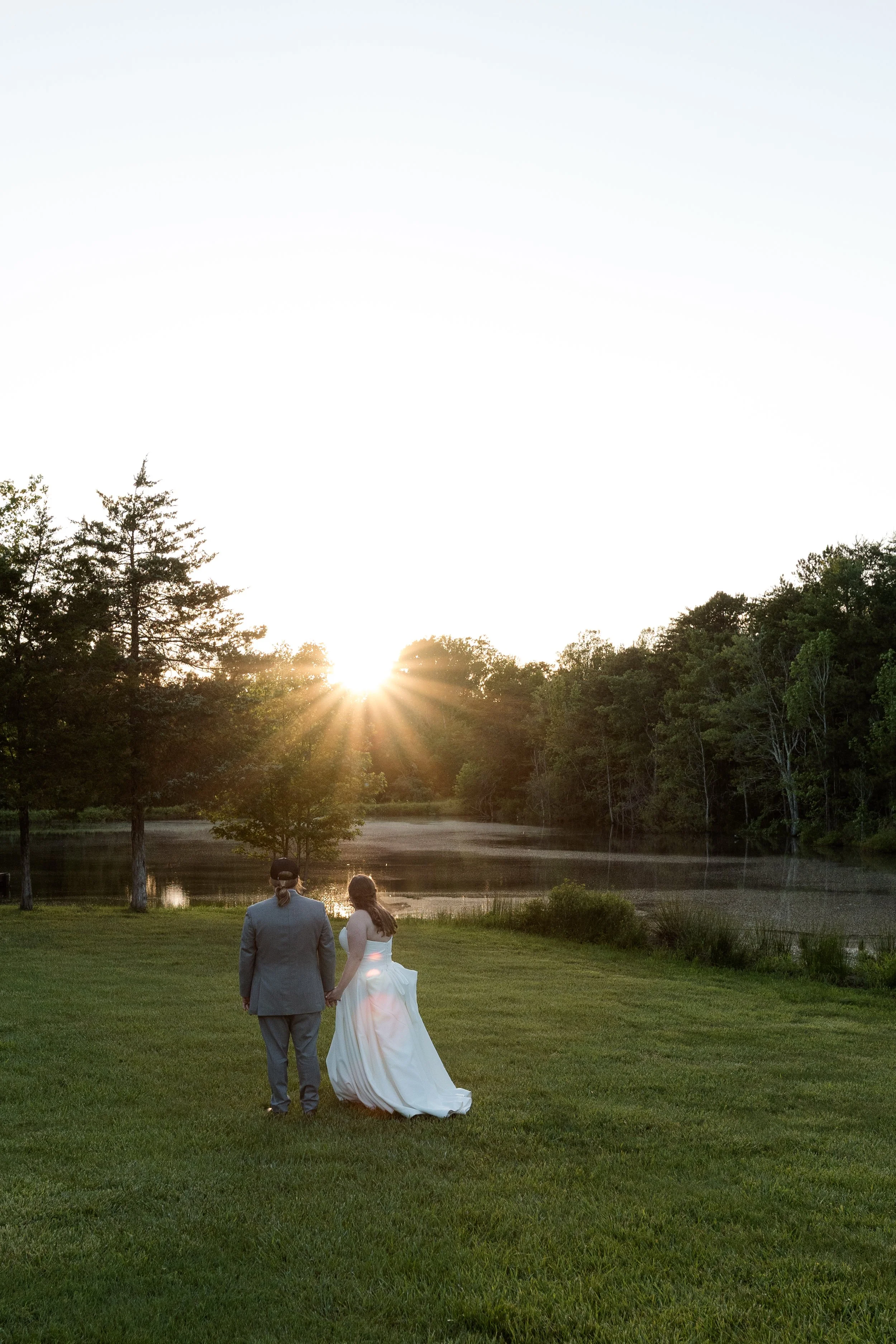 Bride and groom walking hand in hand at sunset by the lake at Persimmon Creek Barn in Beaverdam, Virginia during golden hour wedding portraits.