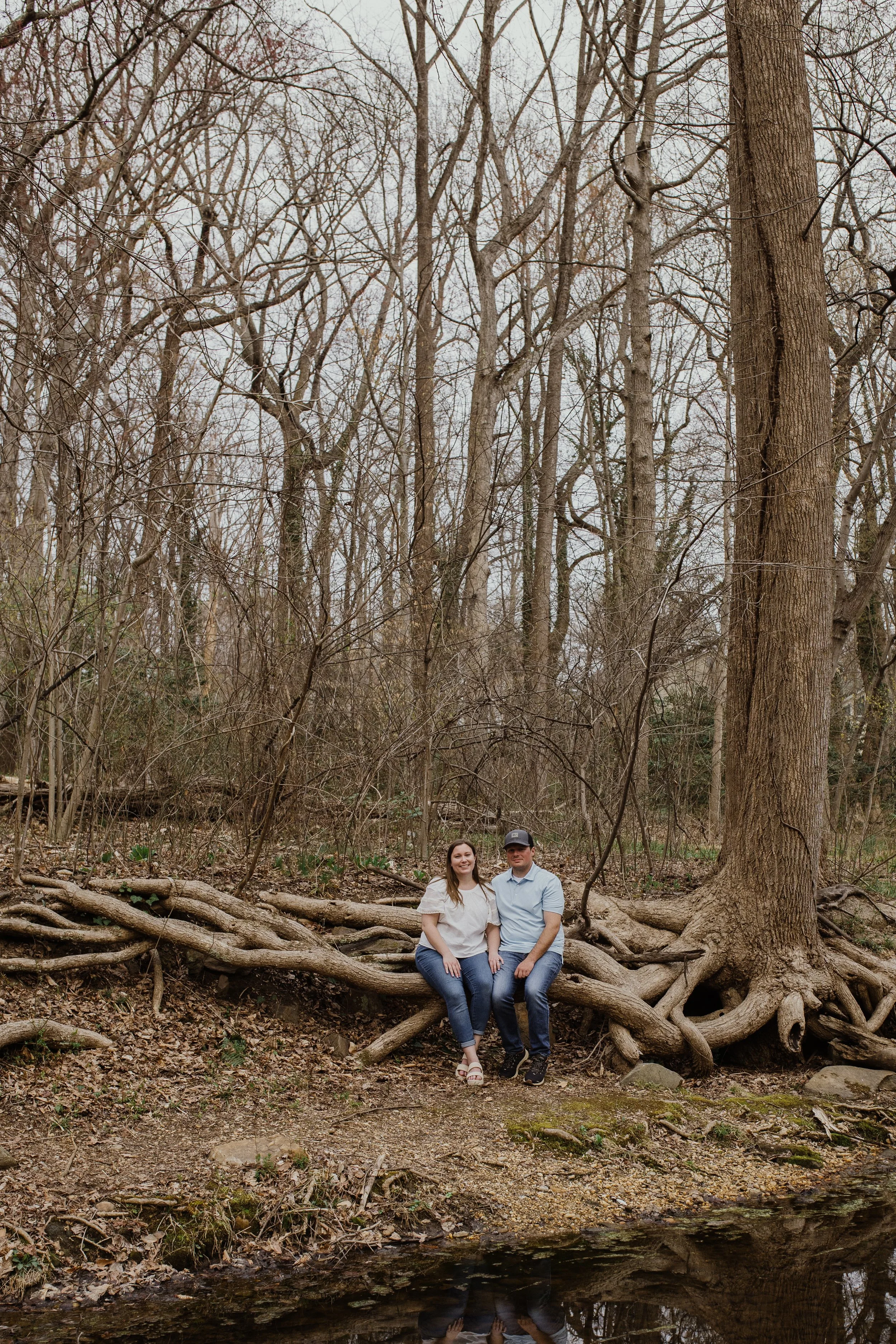 Candid Northern Virginia engagement session with couple sitting by a creek in a natural forest setting.