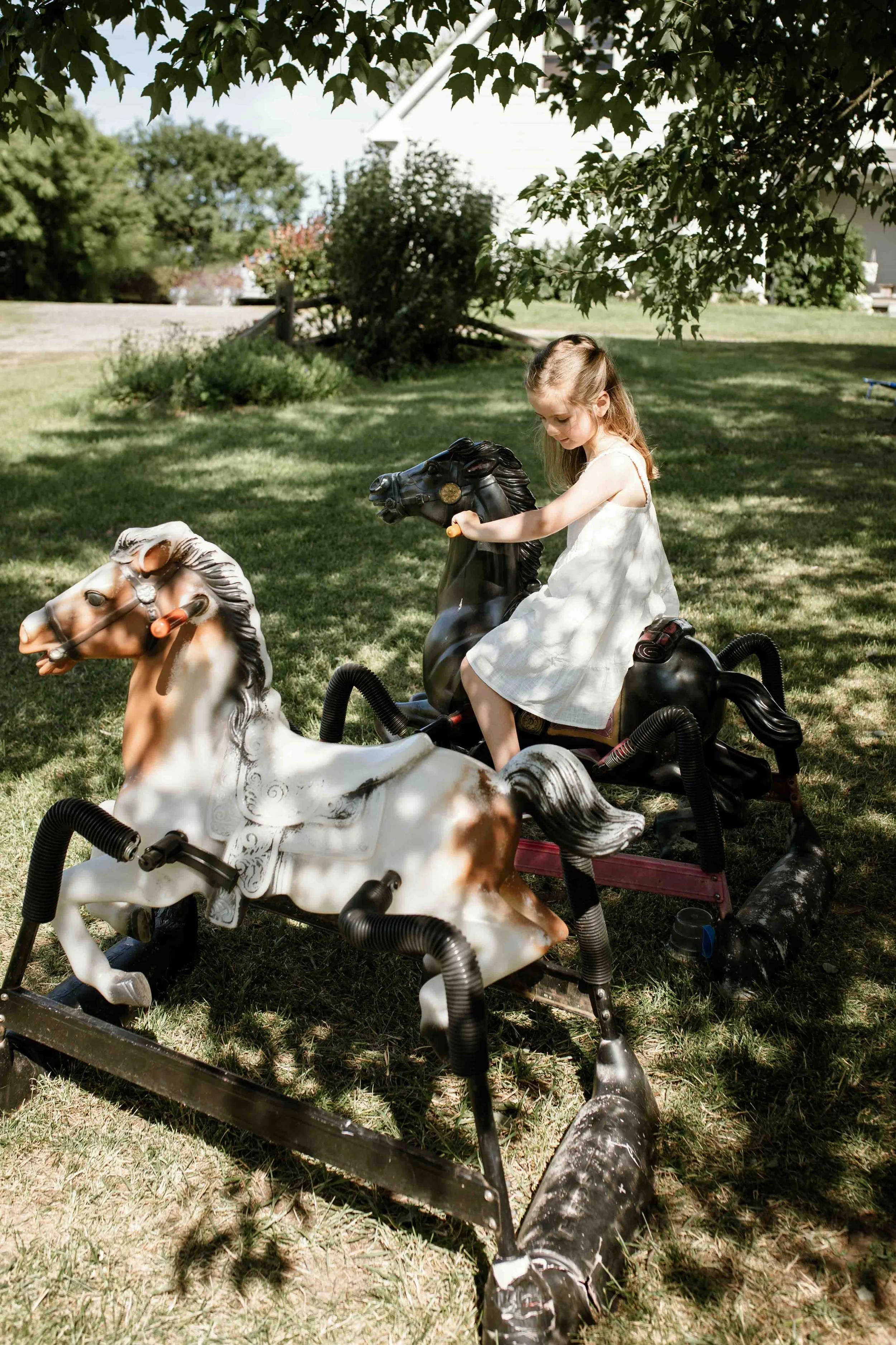 Young girl playing on rocking horse toys during a summer family session at Seven Oaks Lavender Farm in Fauquier County, Virginia.
