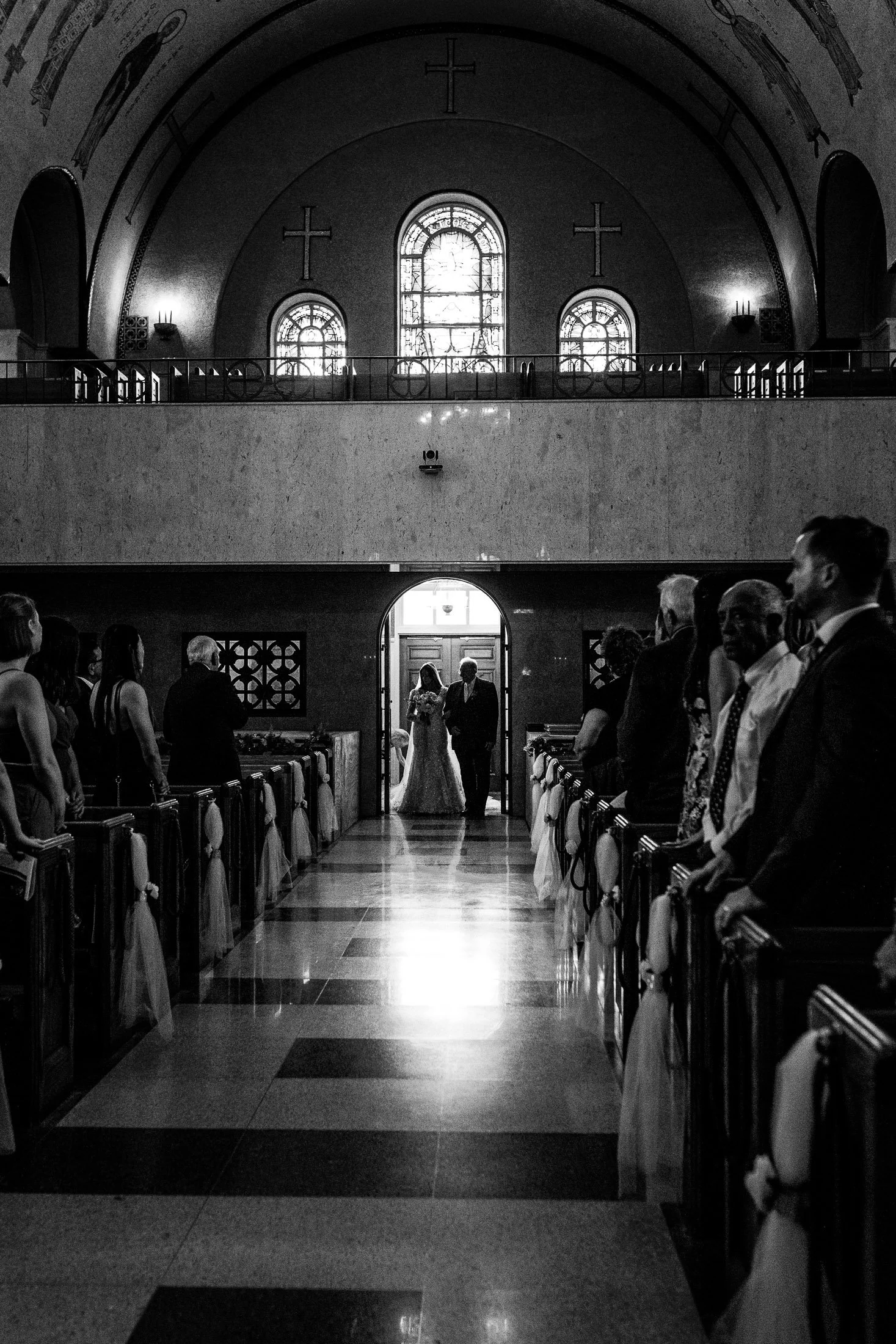 Black and white photo of bride walking down aisle with her father at Saint Sophia Greek Orthodox Cathedral during Greek Orthodox wedding ceremony