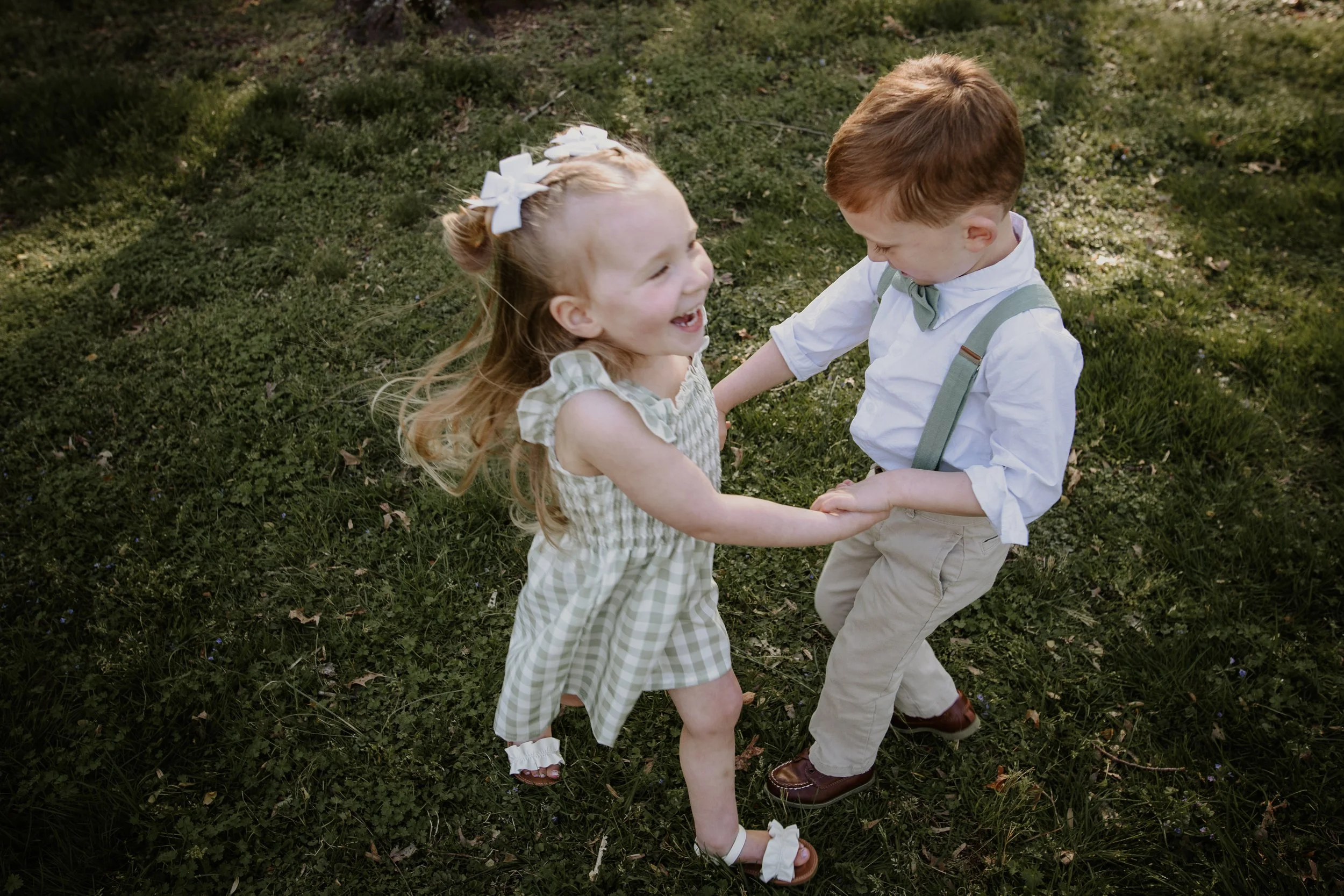 young siblings holding hands and laughing in coordinated green and neutral spring outfits walney park during outdoor family photo session