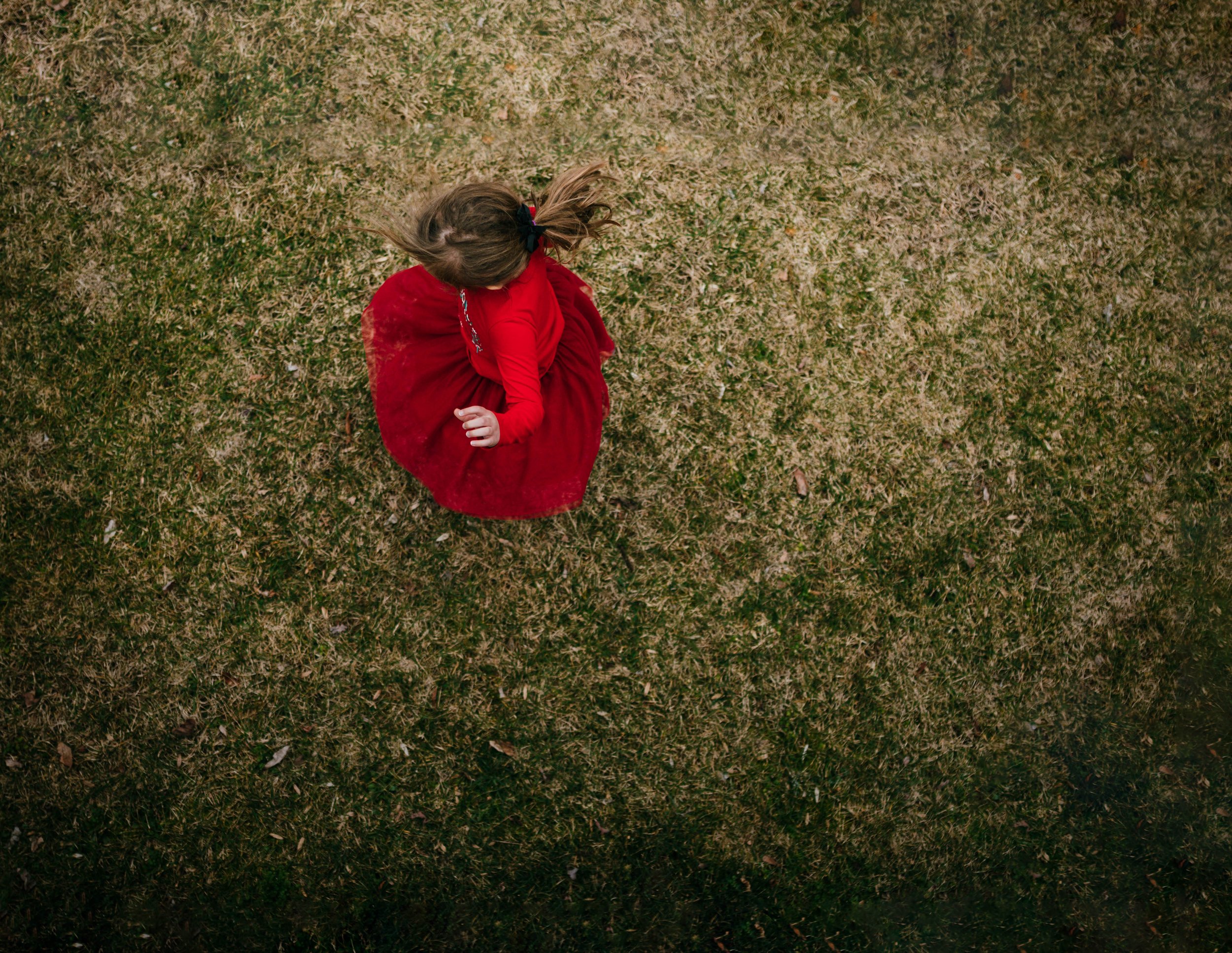 A girl in a red dress sitting on grass viewed from above.