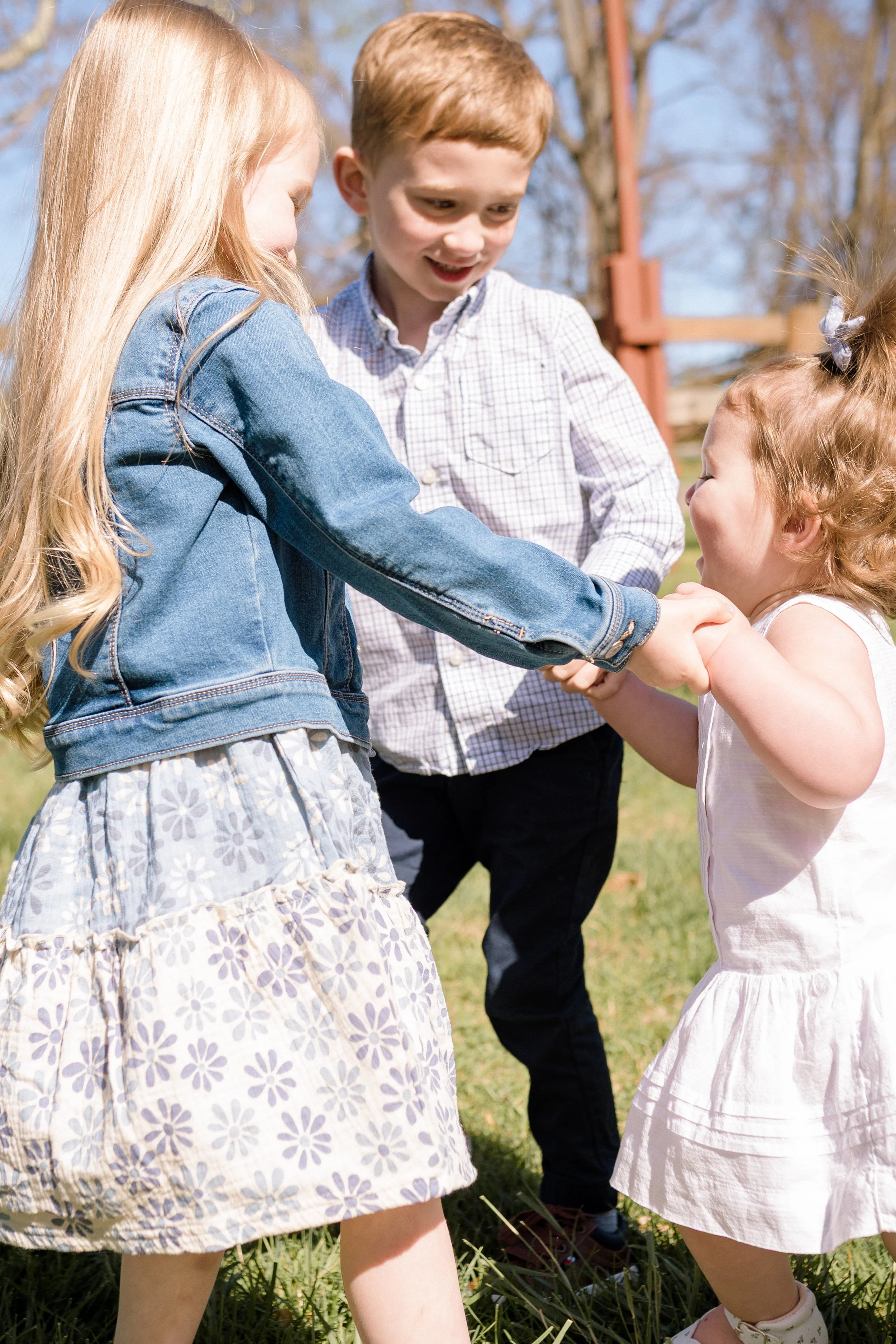 Siblings holding hands and playing together during a bright spring morning family session at Rady Park in Fauquier County.