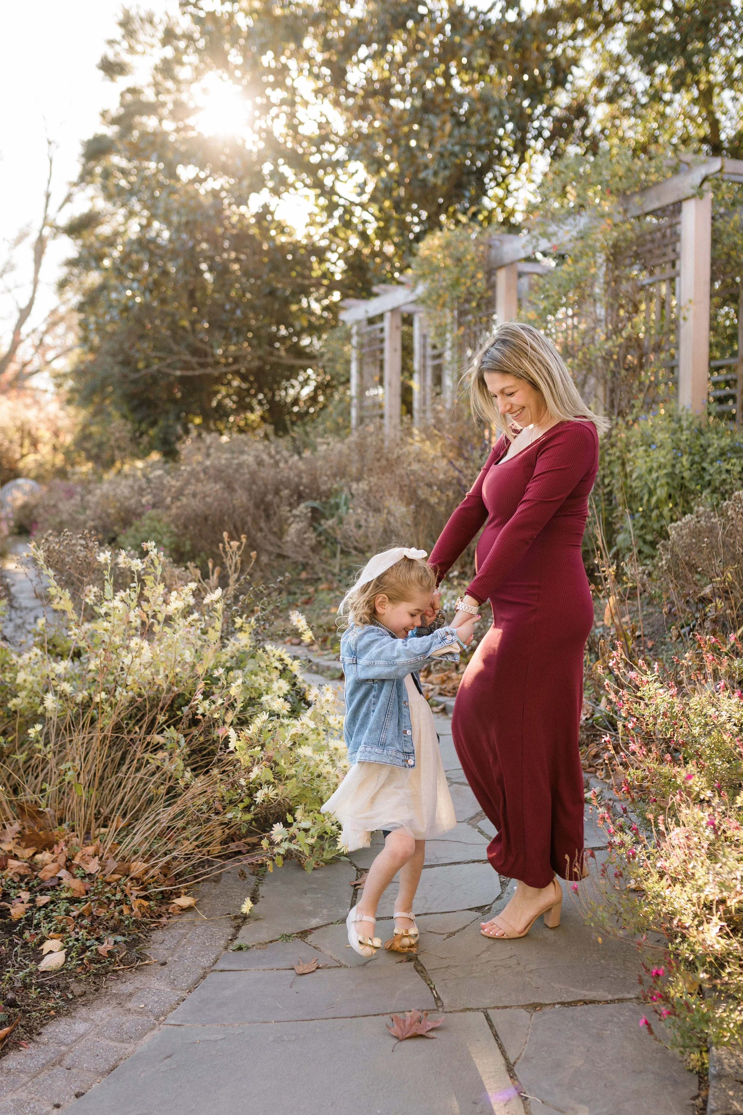 Family and maternity mom and daughter dancing in green spring garden.