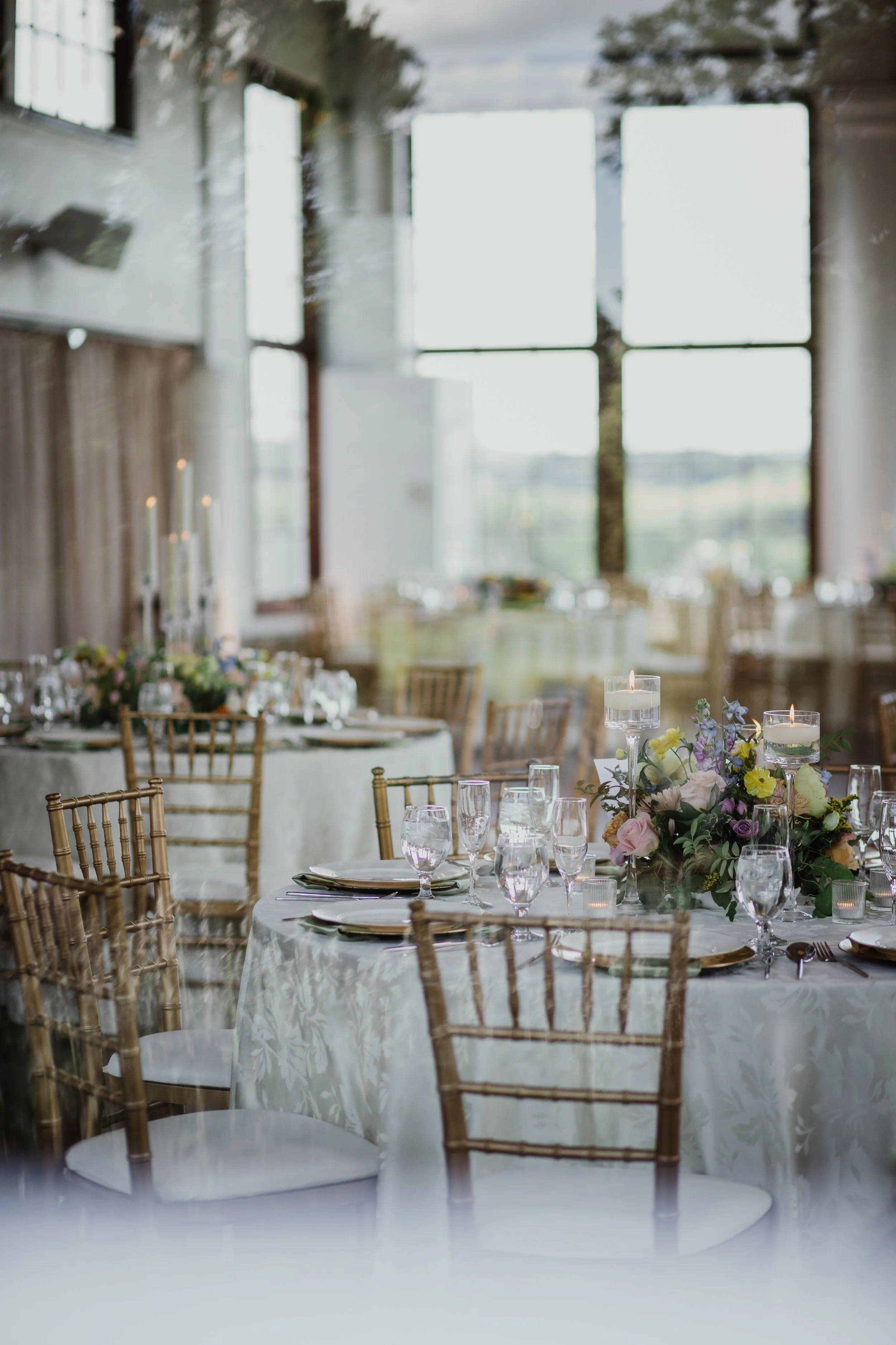 Wedding reception tables and floral centerpieces reflected through glass inside Raspberry Plain Manor in Leesburg, Virginia.