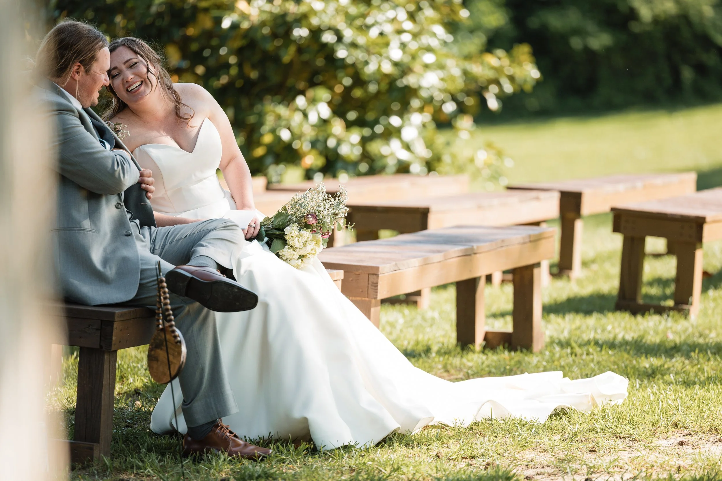 Bride and groom sharing a private vow moment on wooden benches at Persimmon Creek Barn in Beaverdam, Virginia before their outdoor waterfront ceremony.