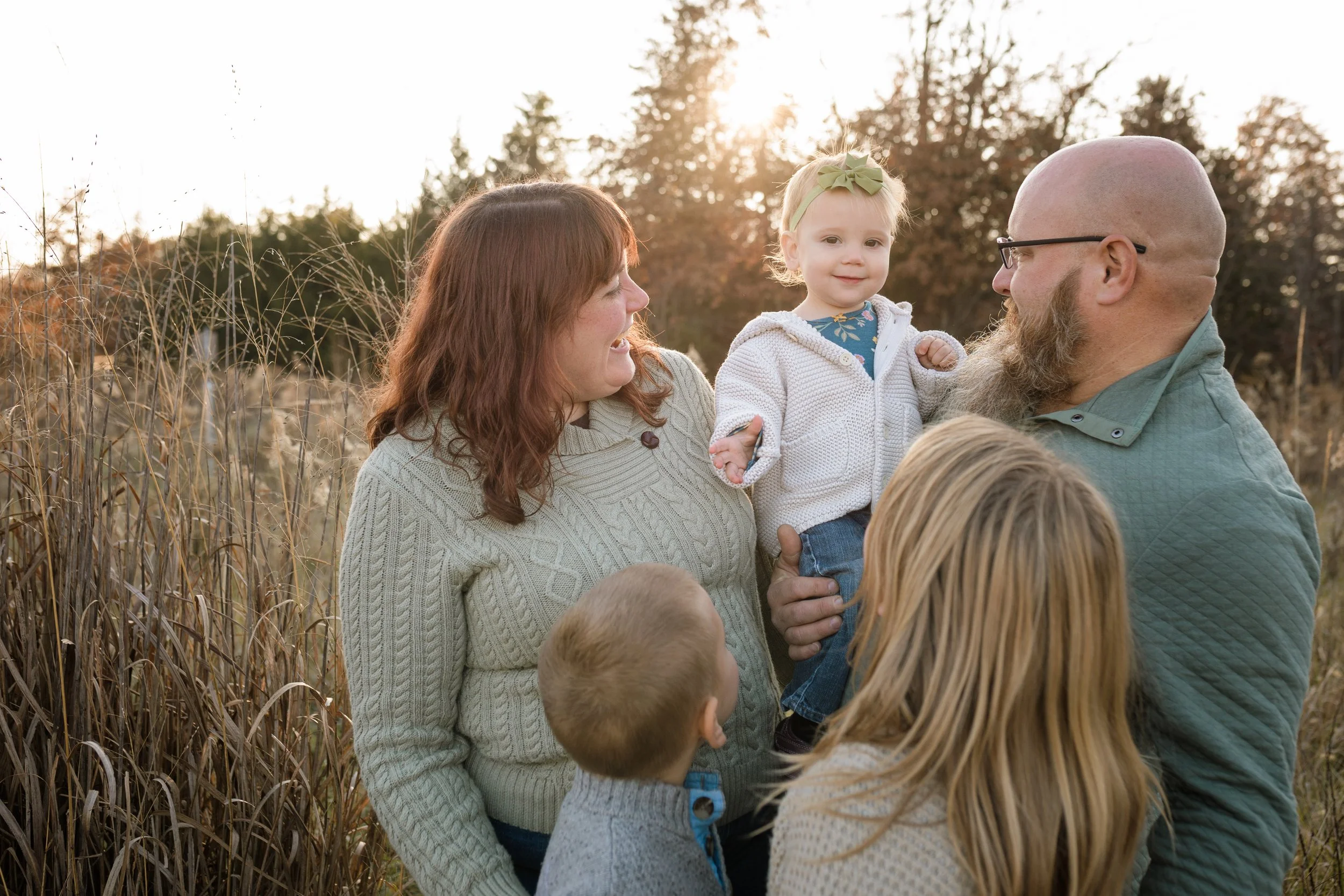 family looking at baby in field at sunset