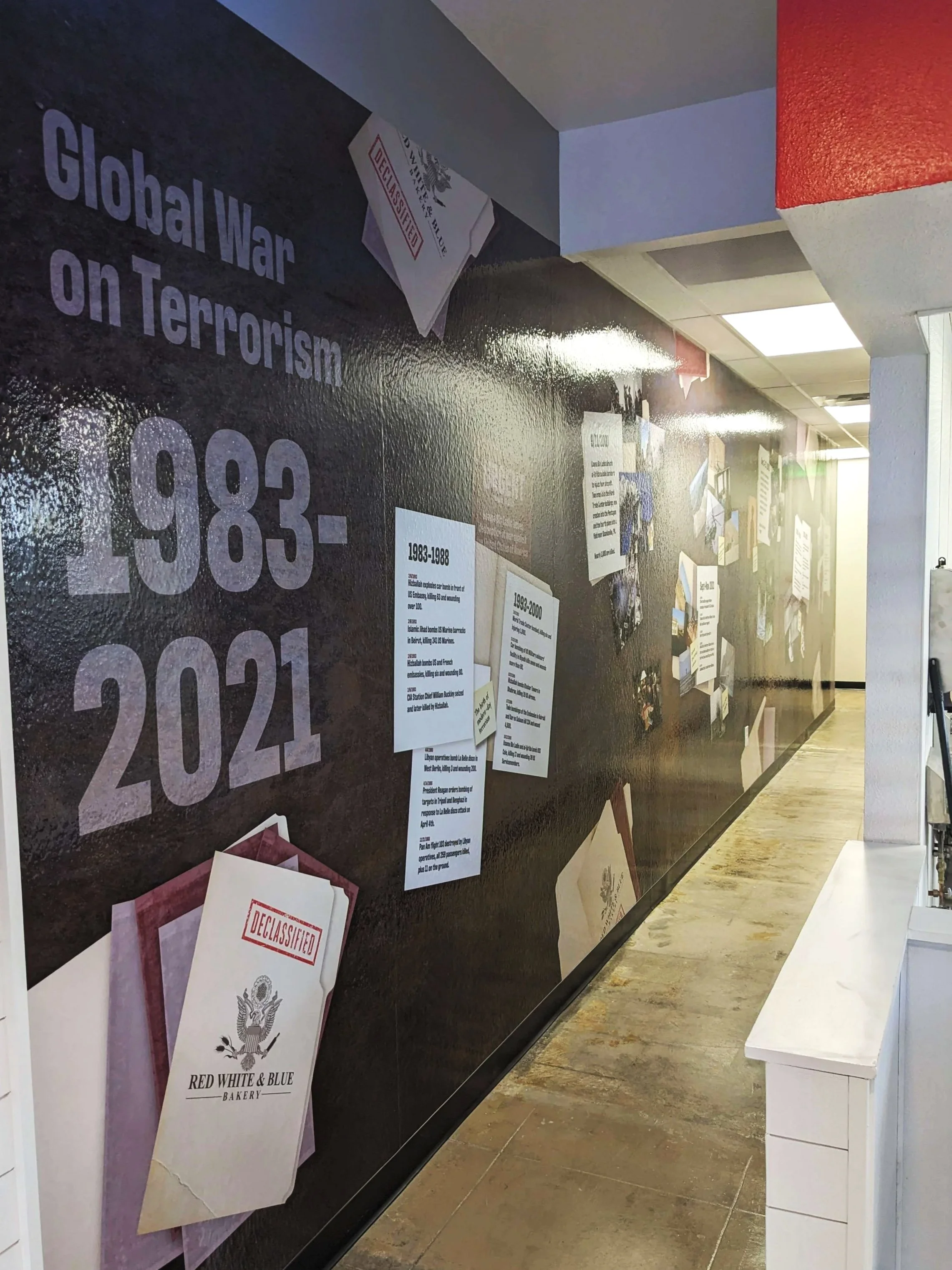 Wall mural depicting the timeline of the Global War on Terrorism from 1983 to 2021 at Red White & Blue Bakery, featuring "declassified" documents and highlighted events.