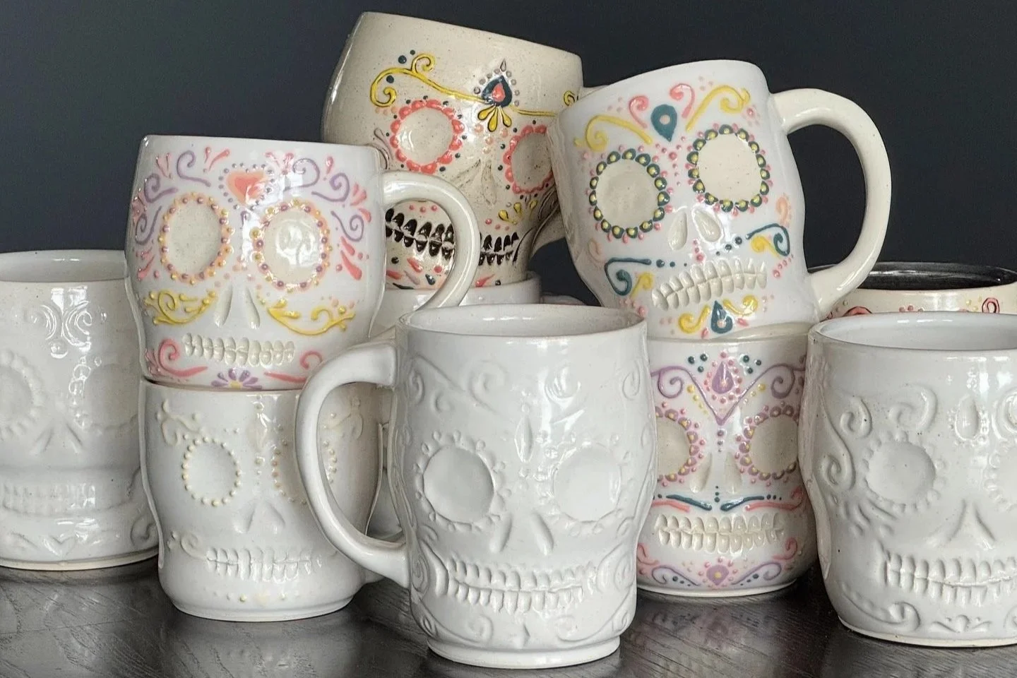 a grouping of stacked up carved skull mugs, some all white, and some decorated in color like sugar skulls on a black background
