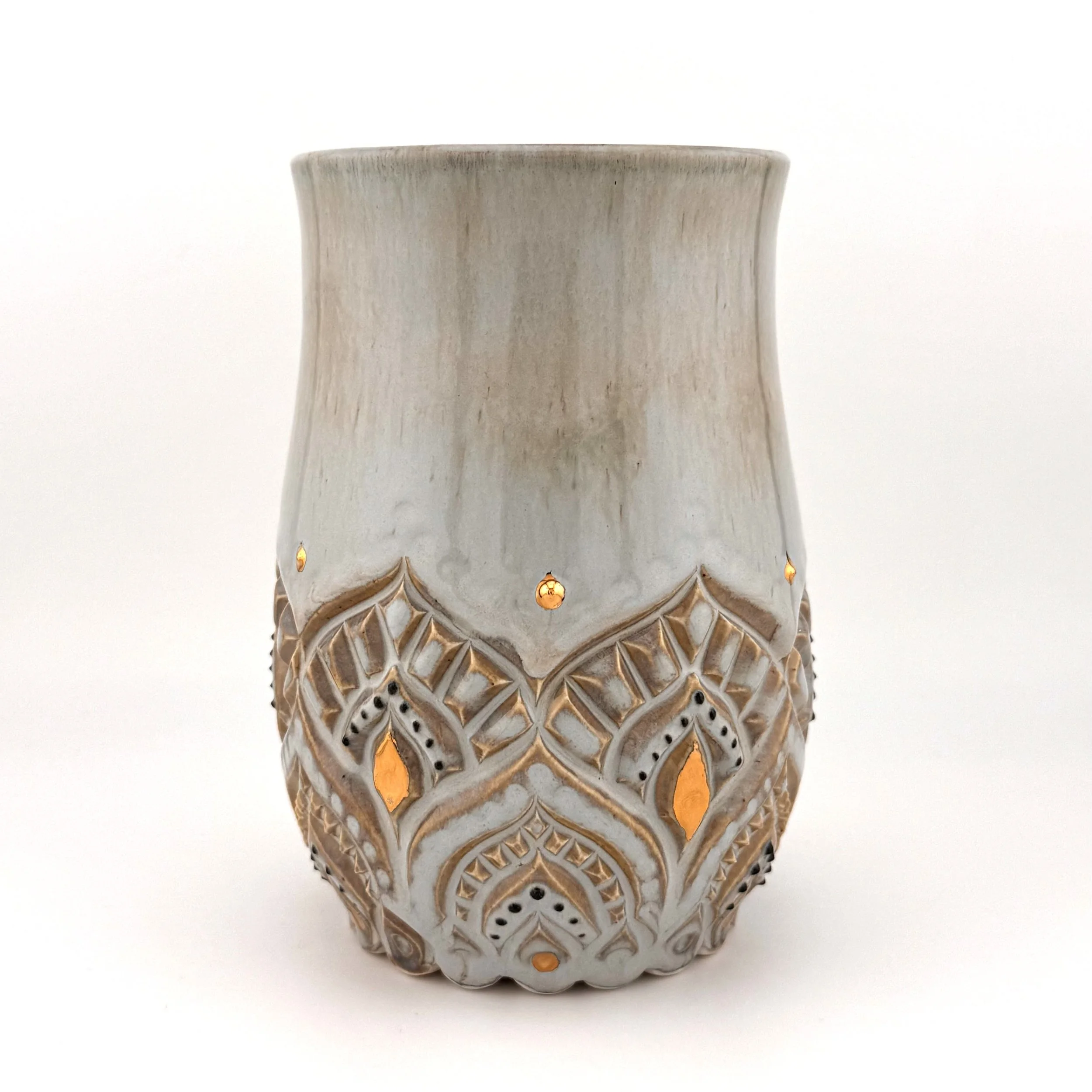 A detailed glazed ceramic vase with intricate carved geometric patterns, decorated with gold accents on a white background.