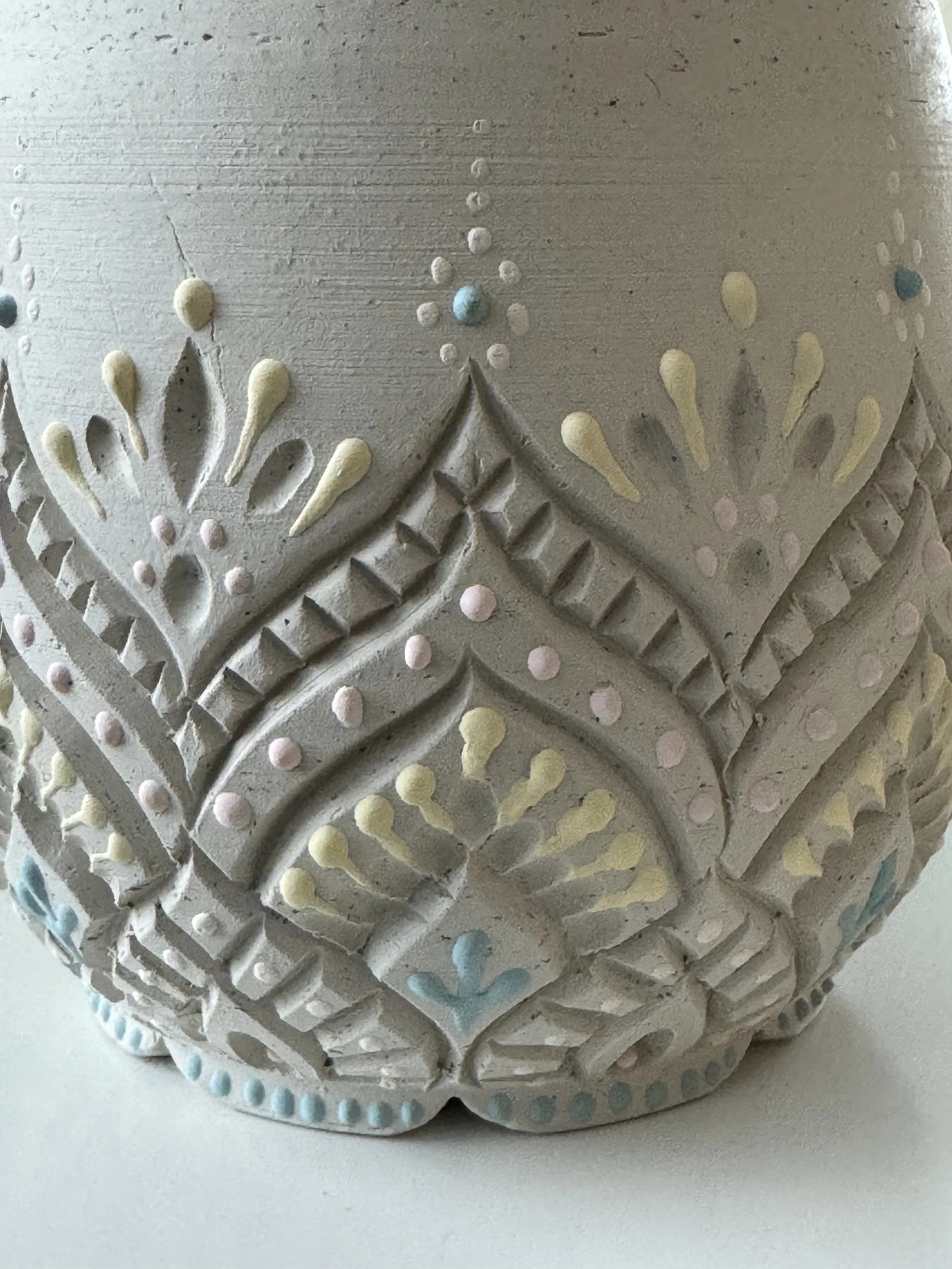 Close-up of an in-progress hand harved and slip trailed ceramic mug with intricate patterns. The slip details are multi-colored in yellow, pink, and teal.