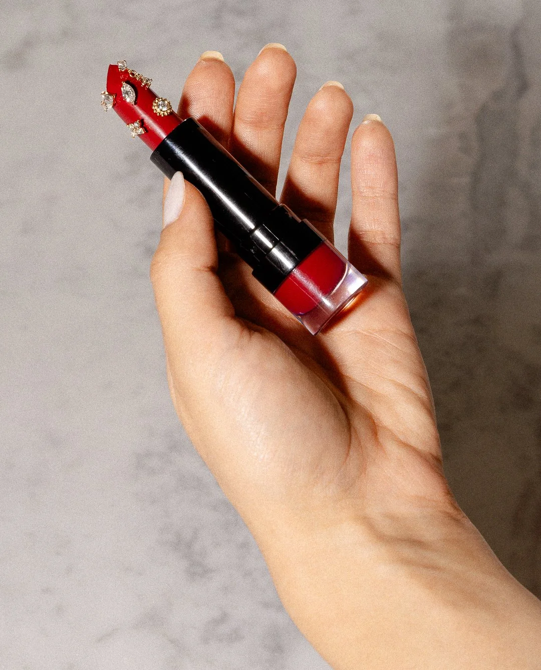 Hand holding a lipstick tube with the top shaped like a red lipstick with jewelry accents.