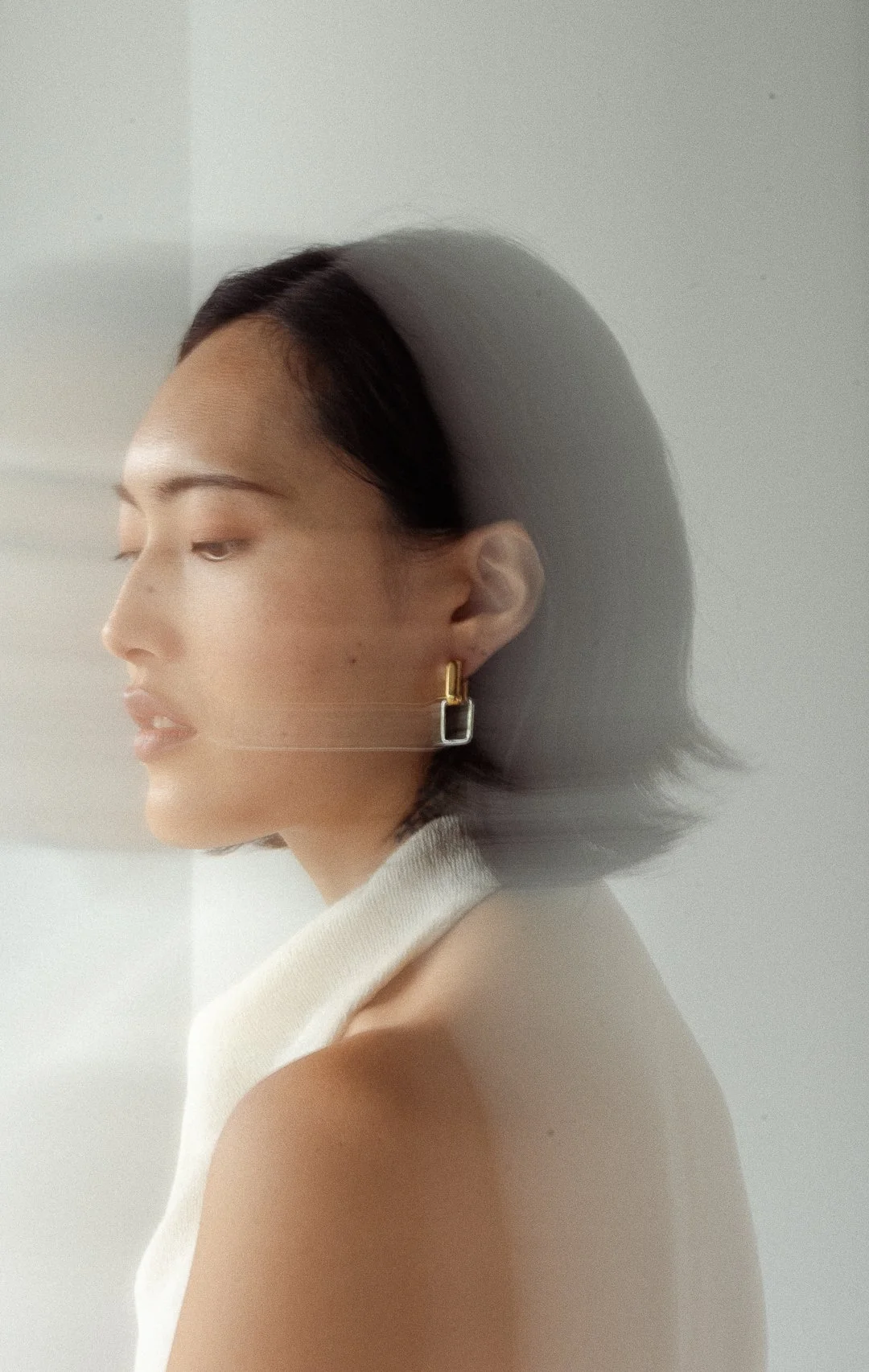 A woman with short dark hair and a patterned earring looking to the side, with a shadow cast on the wall behind her.