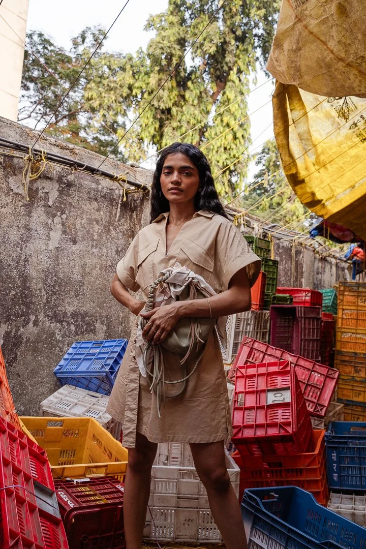 A woman standing among colorful plastic crates and containers, outdoors on a sunny day with trees in the background.