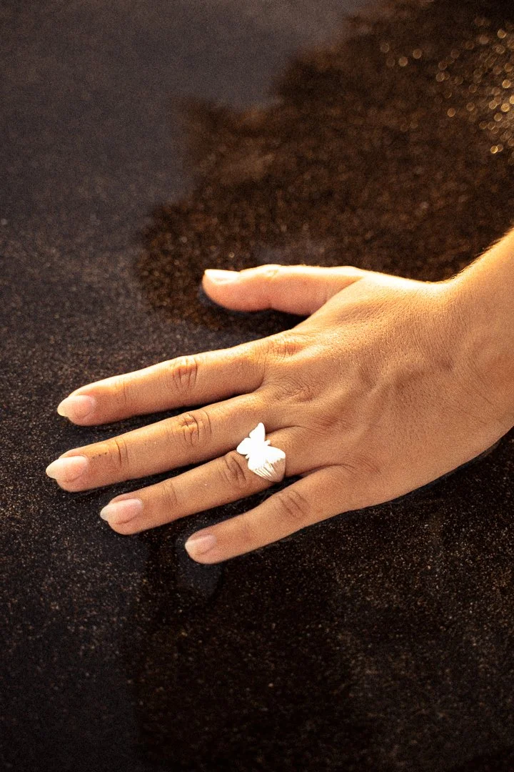 A hand resting on a dark, speckled surface, wearing a white butterfly-shaped ring.