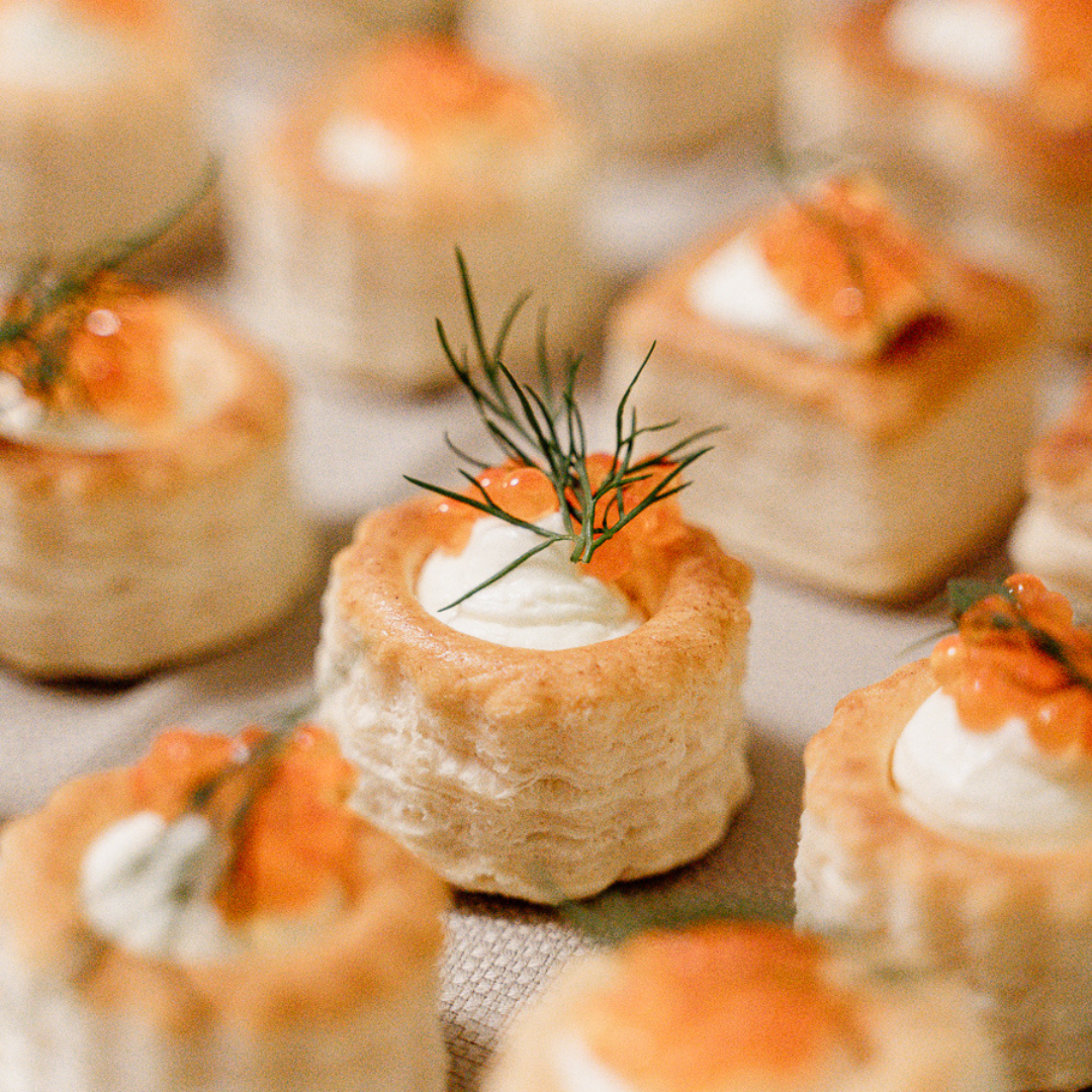 Miniature savory tarts topped with cream, orange sauce, and a sprig of dill.