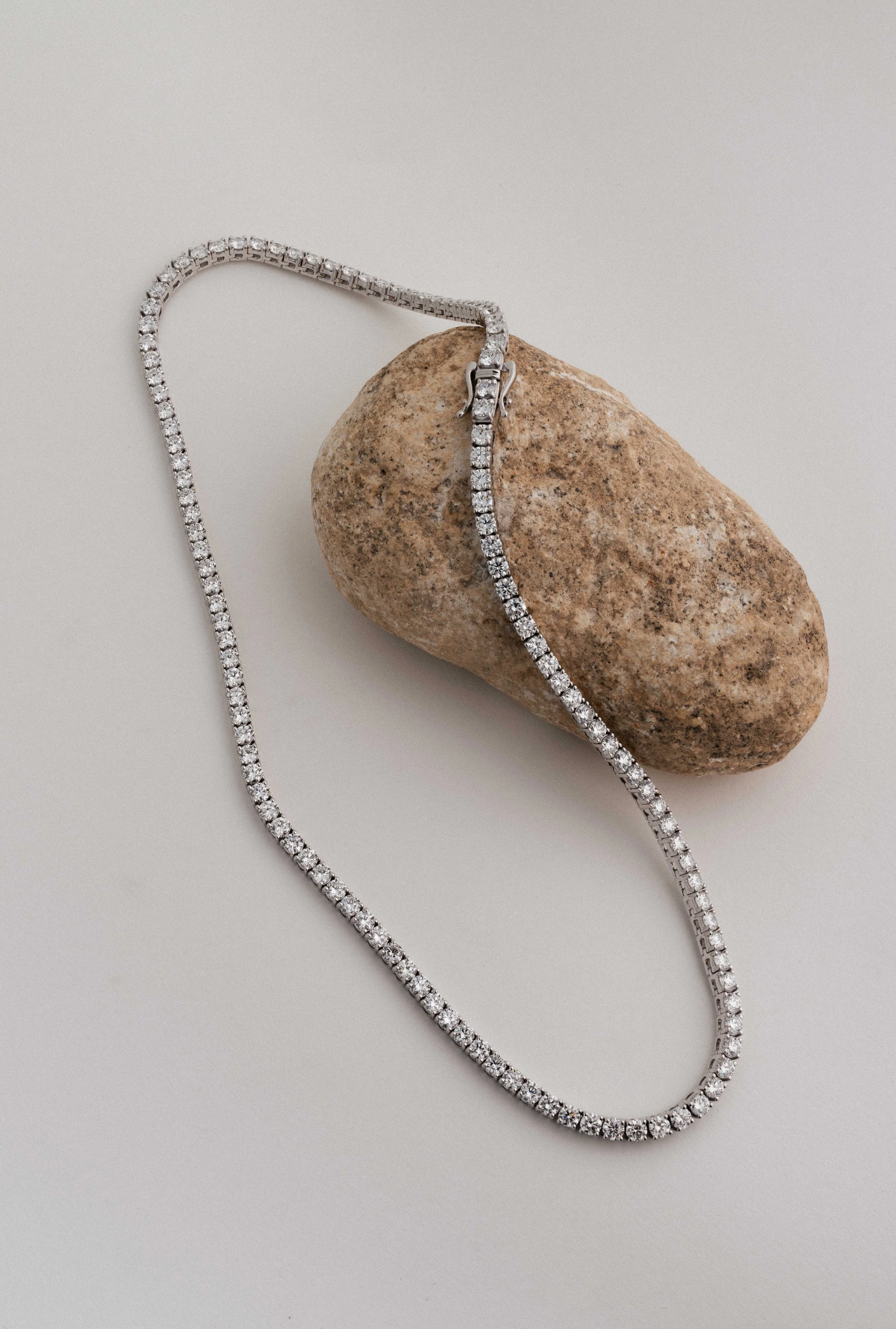 A diamond necklace draped over a smooth brown stone on a light-colored surface.