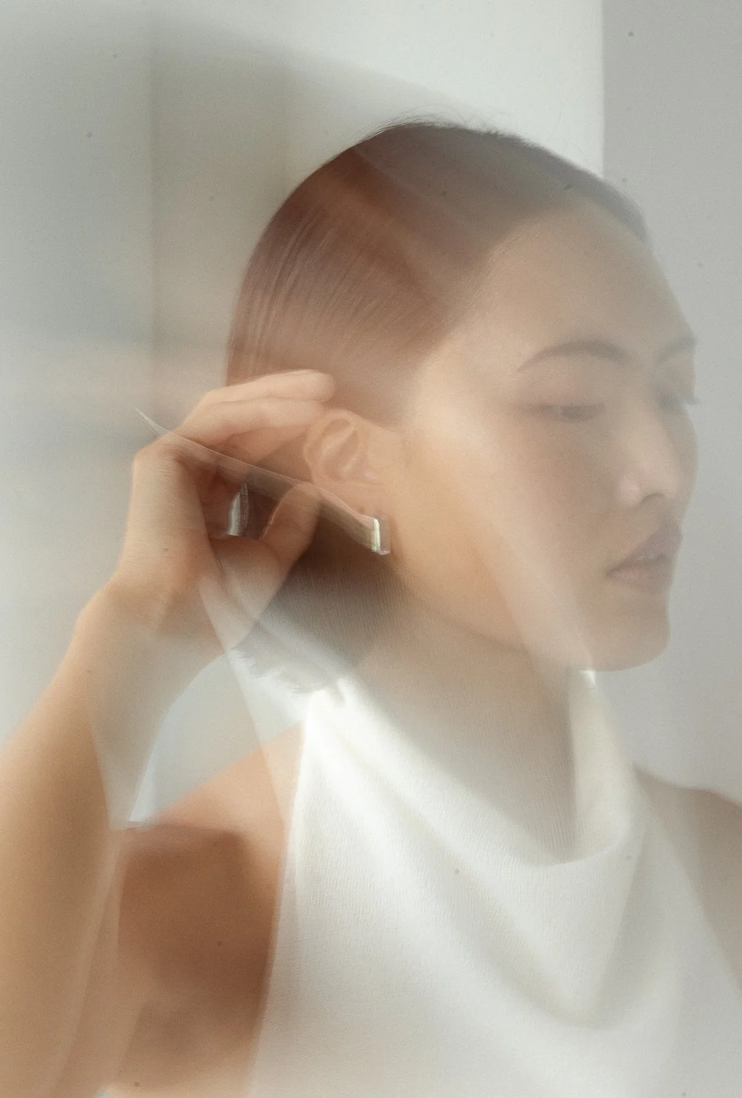 A woman with straight hair combs her hair by a mirror with a soft focus or reflection effect.