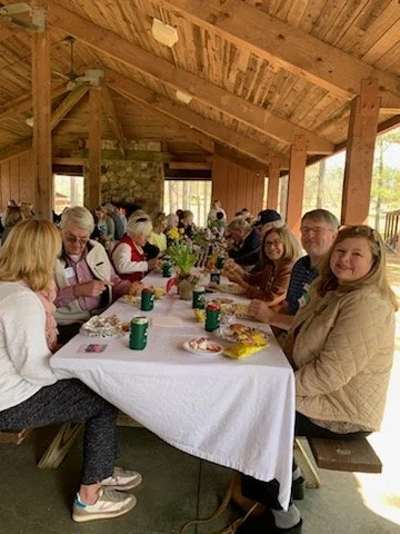 People gathered around a long table under a covered outdoor pavilion, enjoying a meal together.