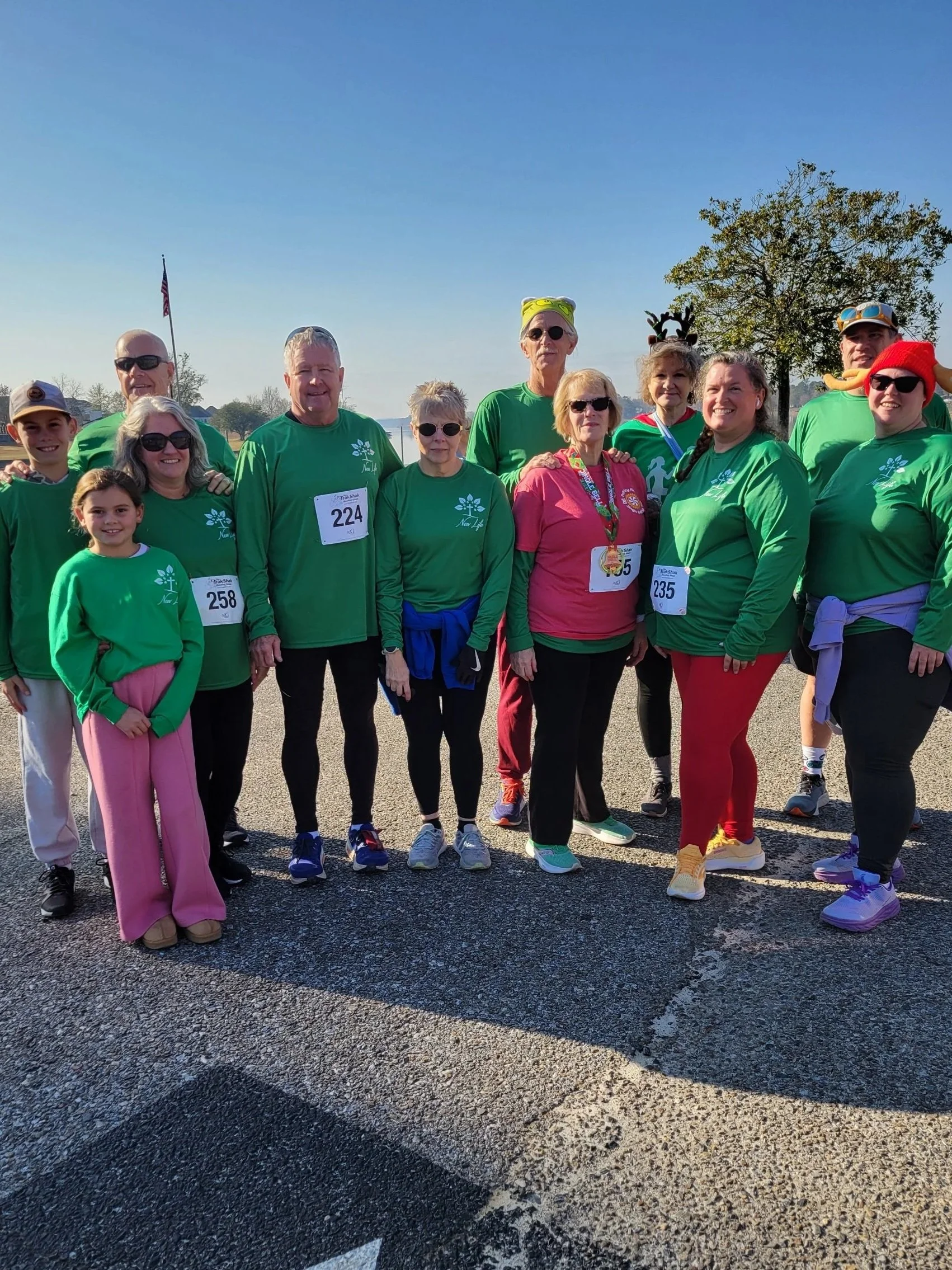 Group of people dressed in green shirts participating in a charity run or walk event outdoors on a sunny day.