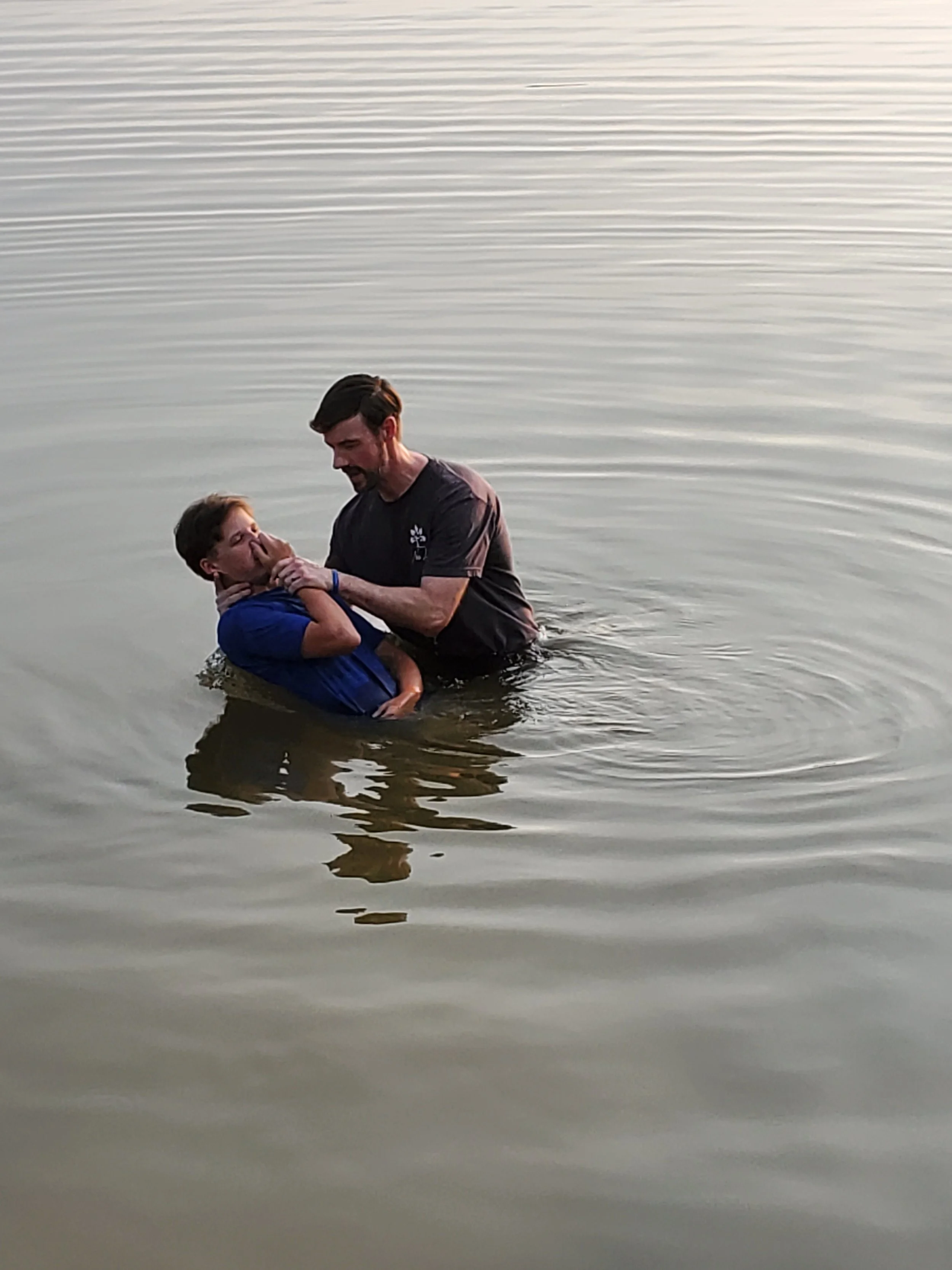 A man baptizing a boy in a body of water during sunset or sunrise.