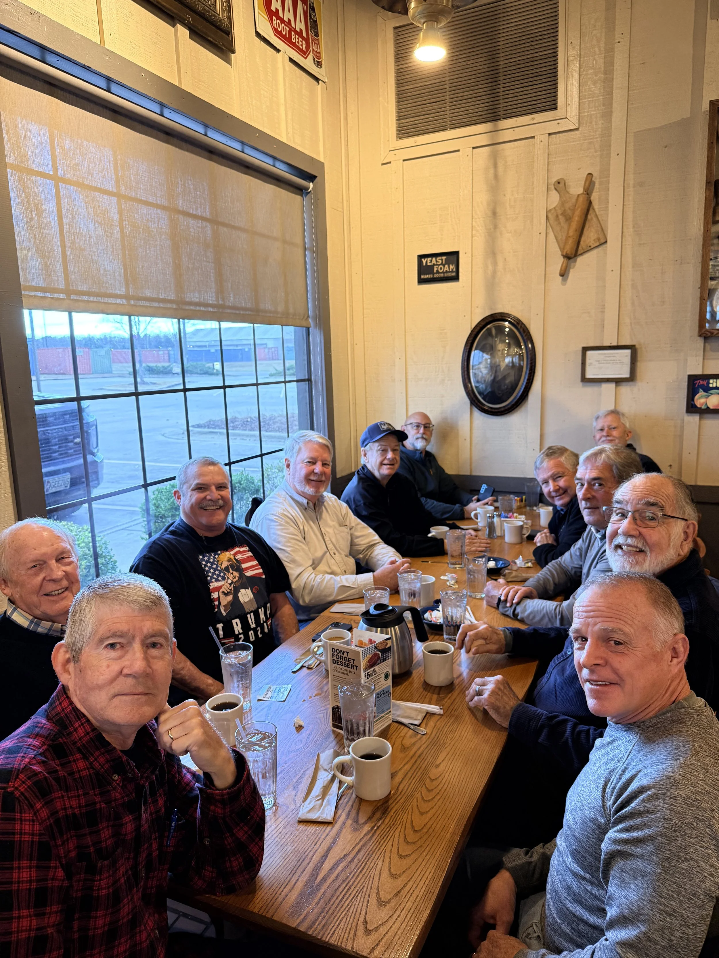 A group of men sitting around a long wooden table inside a cozy cafe or restaurant, enjoying coffee and good company.