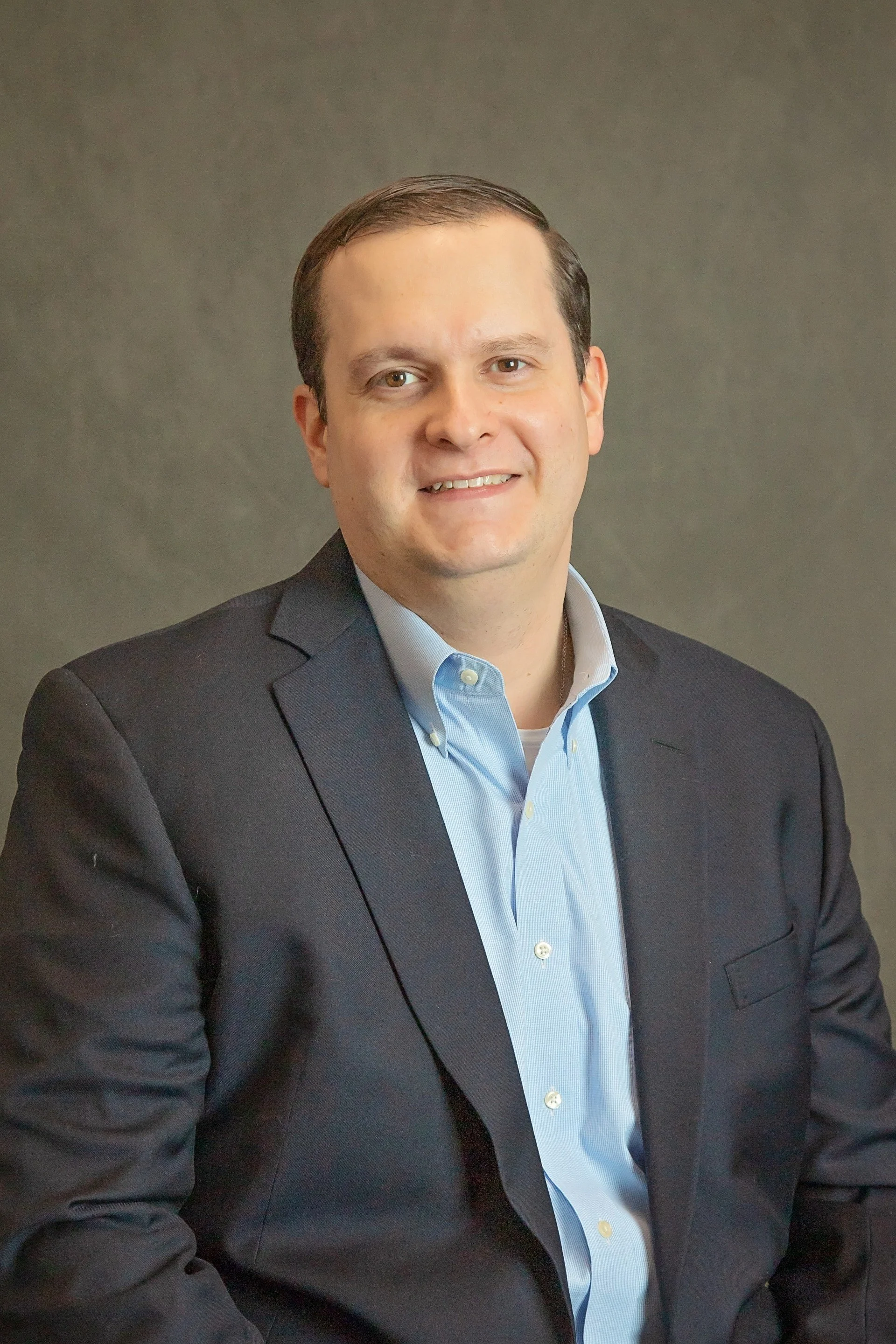 A man in a suit smiling against a plain background.