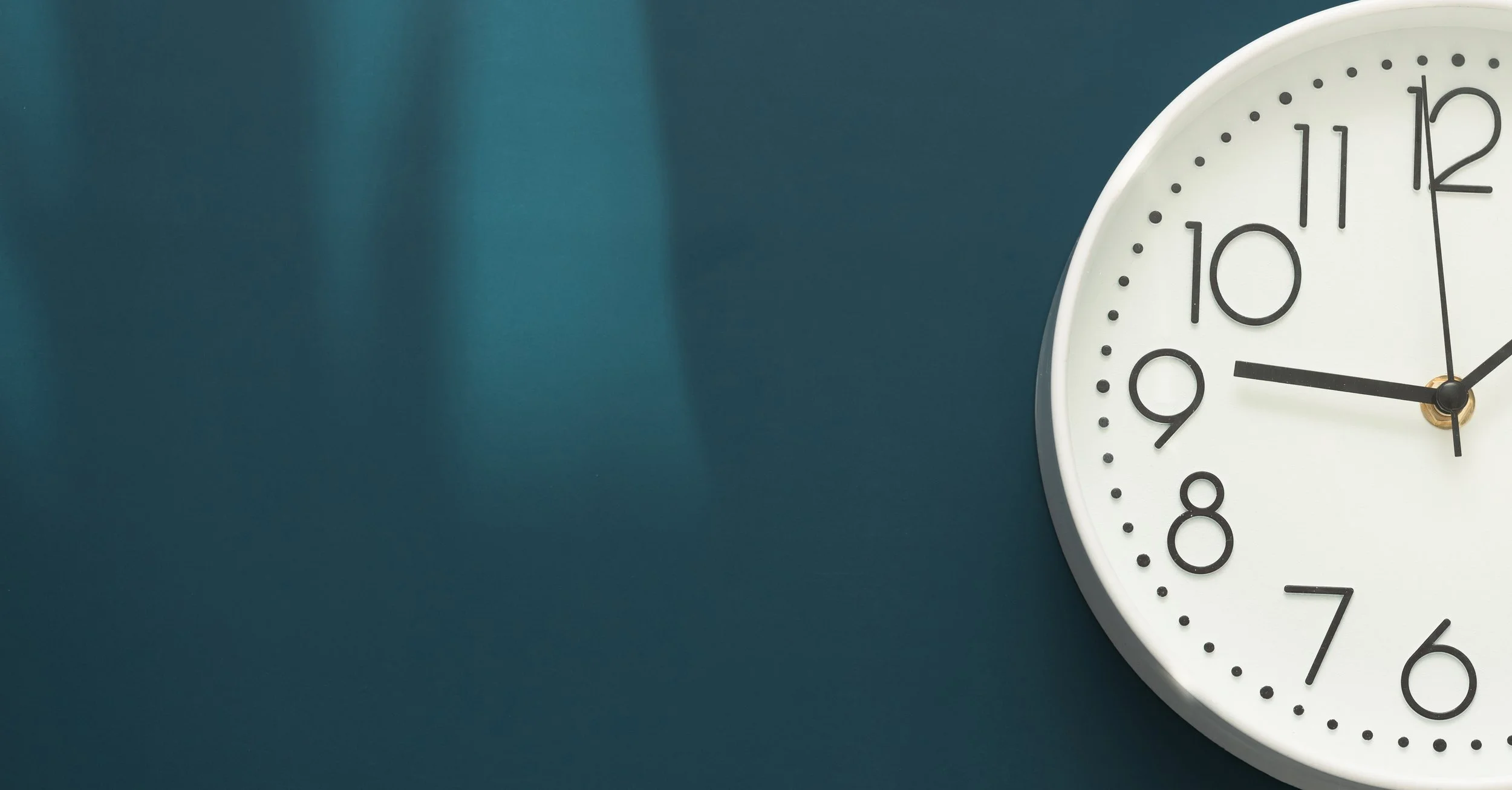 White clock hung on a teal wall that reads 9:59.