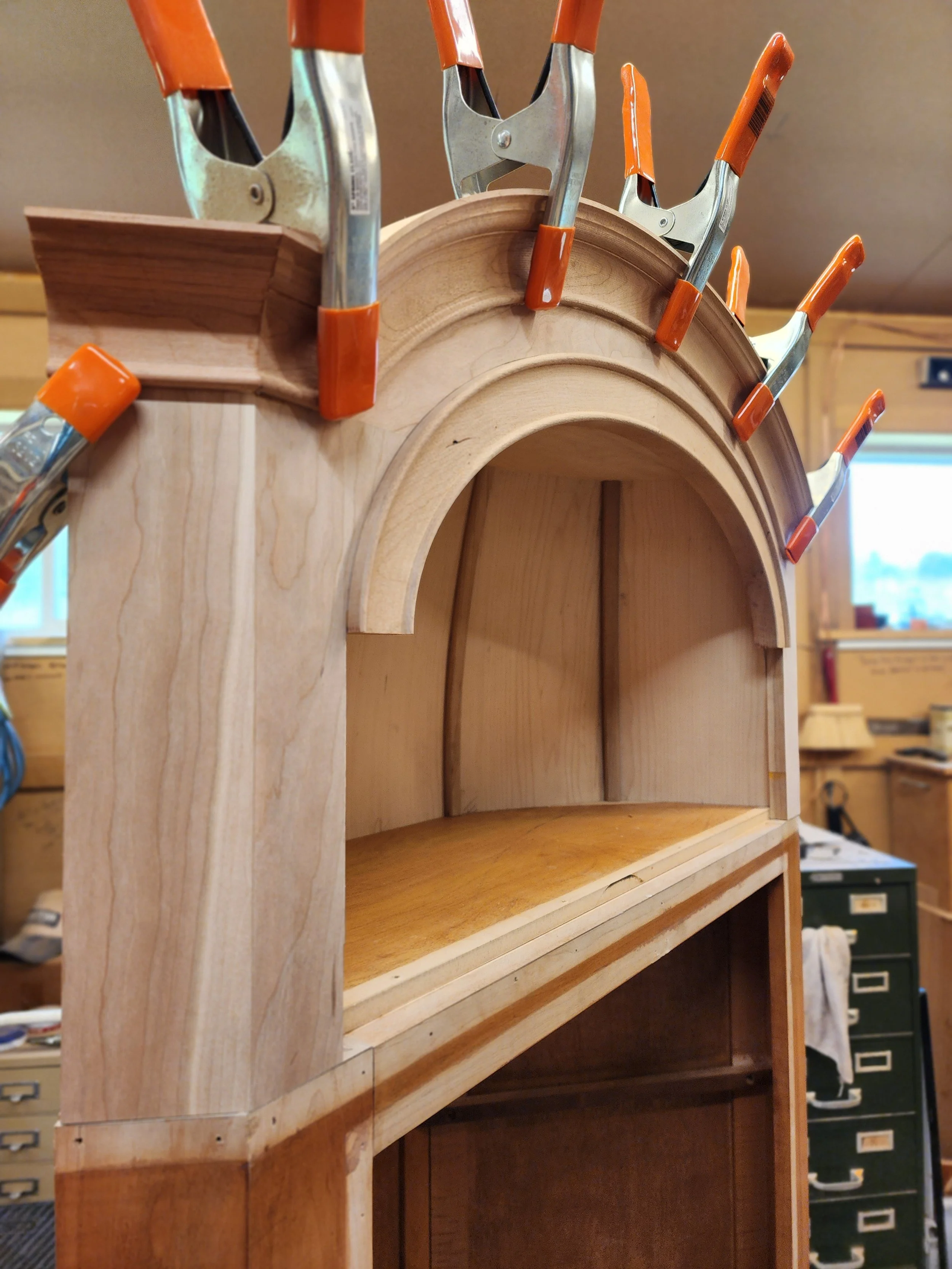 Assembly of coopered solid cherry and maple veneer corner cabinet with beaded solid wood crown detail