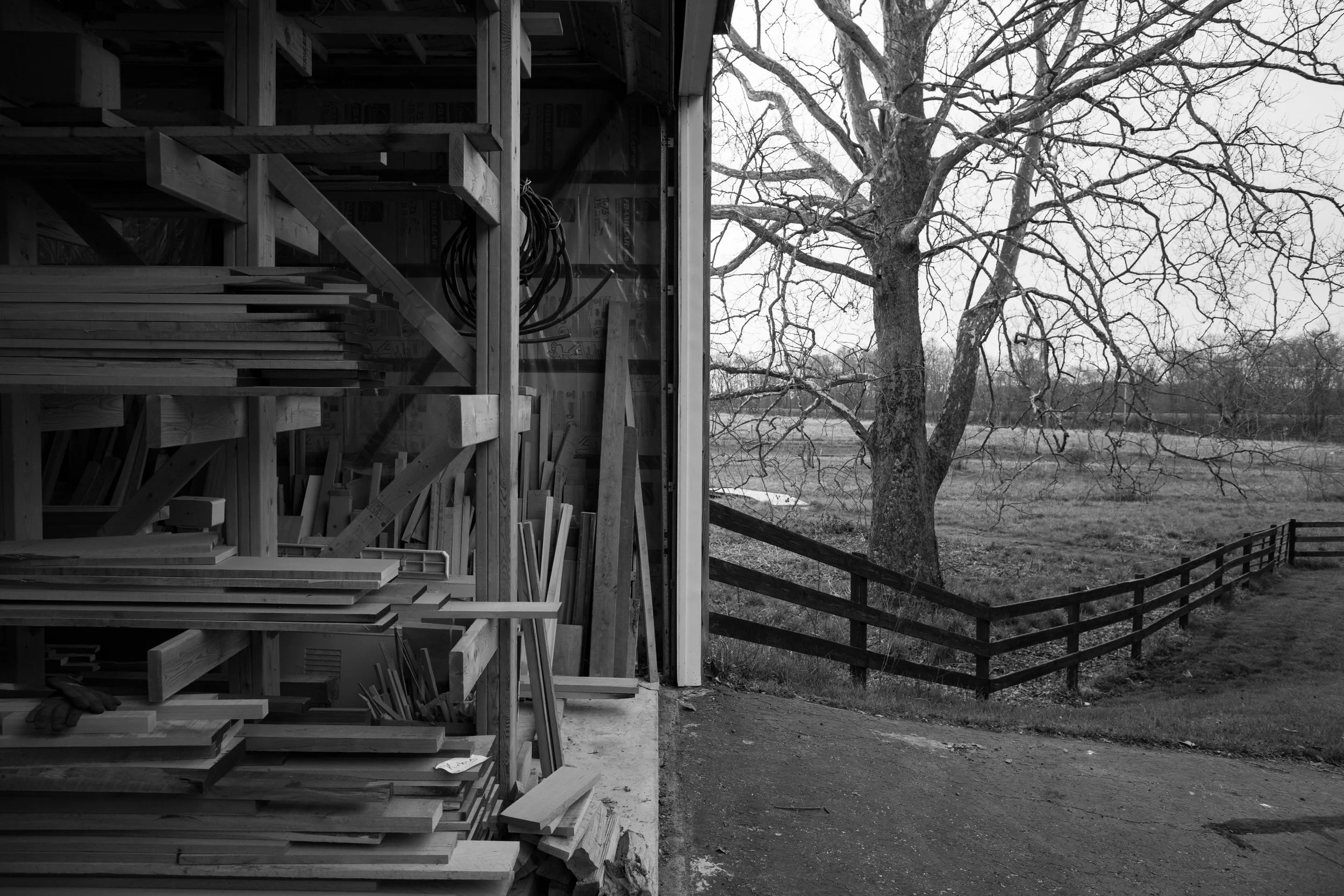 Mixed lumber for custom furniture selection featured in woodshop with open shop door showing adjacent sycamore tree