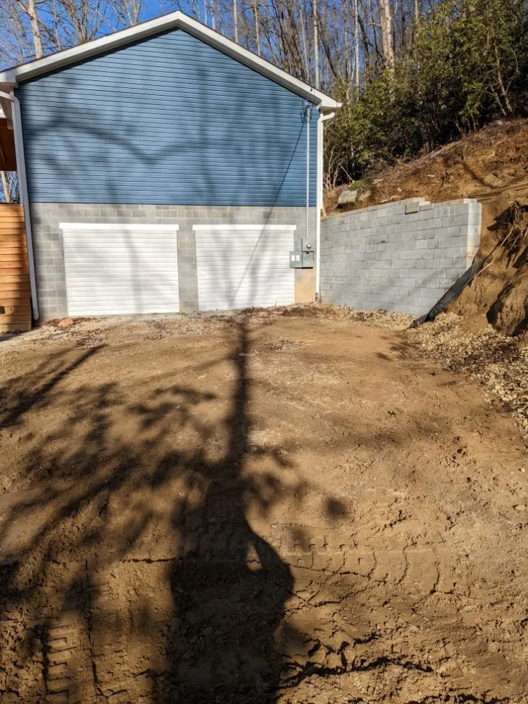 View from exterior of 2 car garage with 2 doors. Garage is a smokey blue color with gray brick and white doors. 