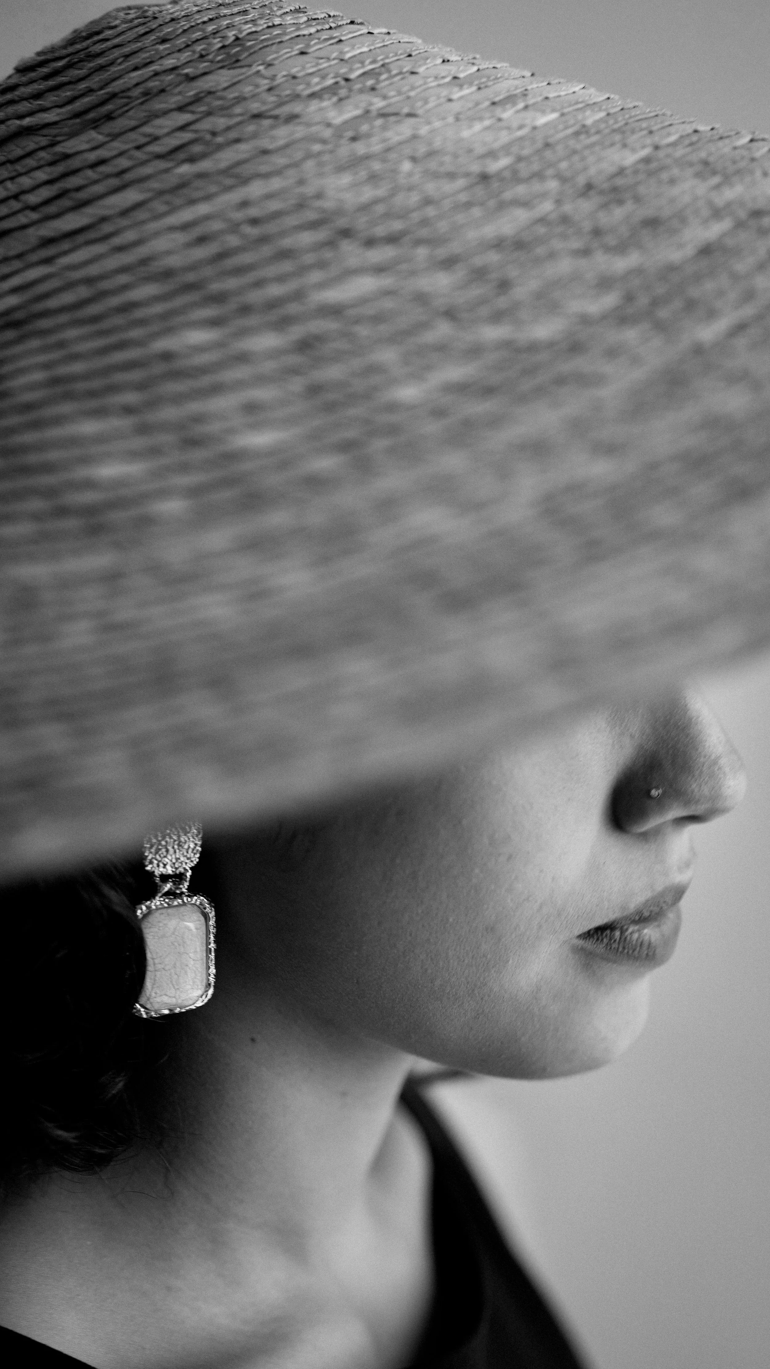 Retrato en blanco y negro de una mujer con sombrero de ala grande que cubre parte de su rostro, usando un pendiente grande.