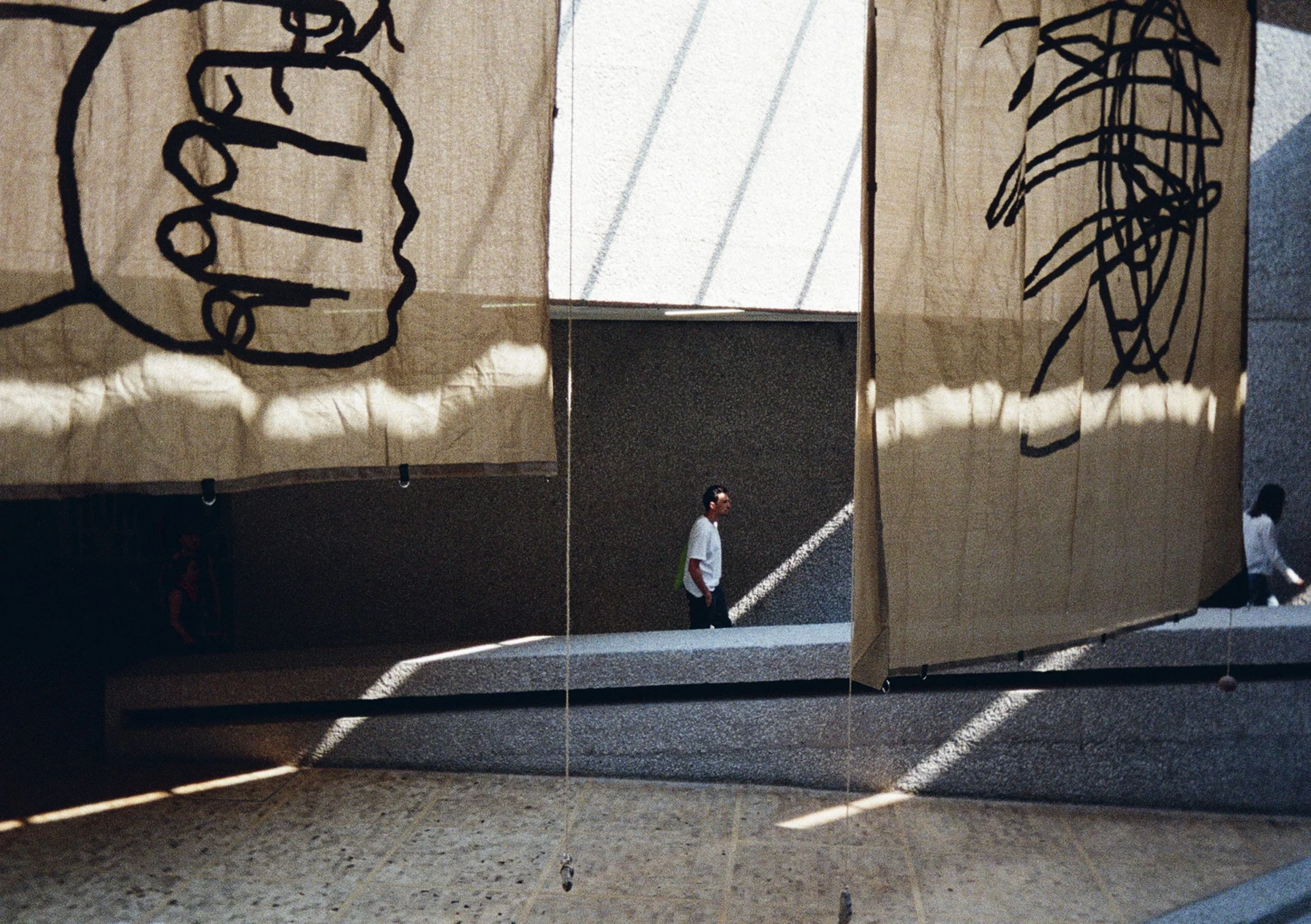 Personas caminando en un espacio cubierto decorado con telañas con dibujos abstractos colgadas