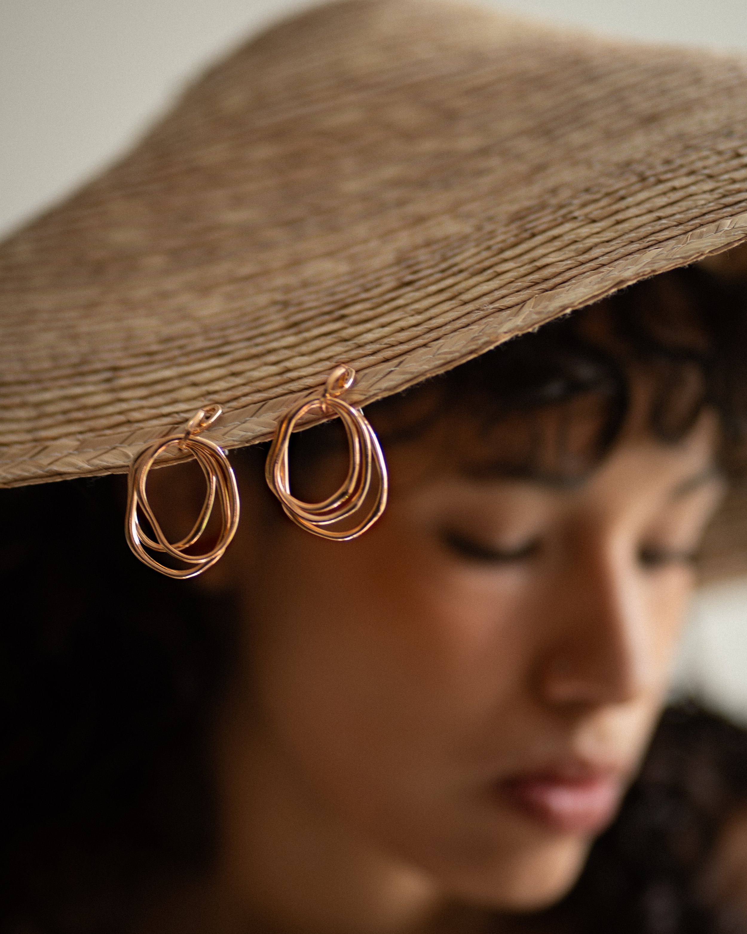 Mujer con sombrero de paja y pendientes de aro rosados.
