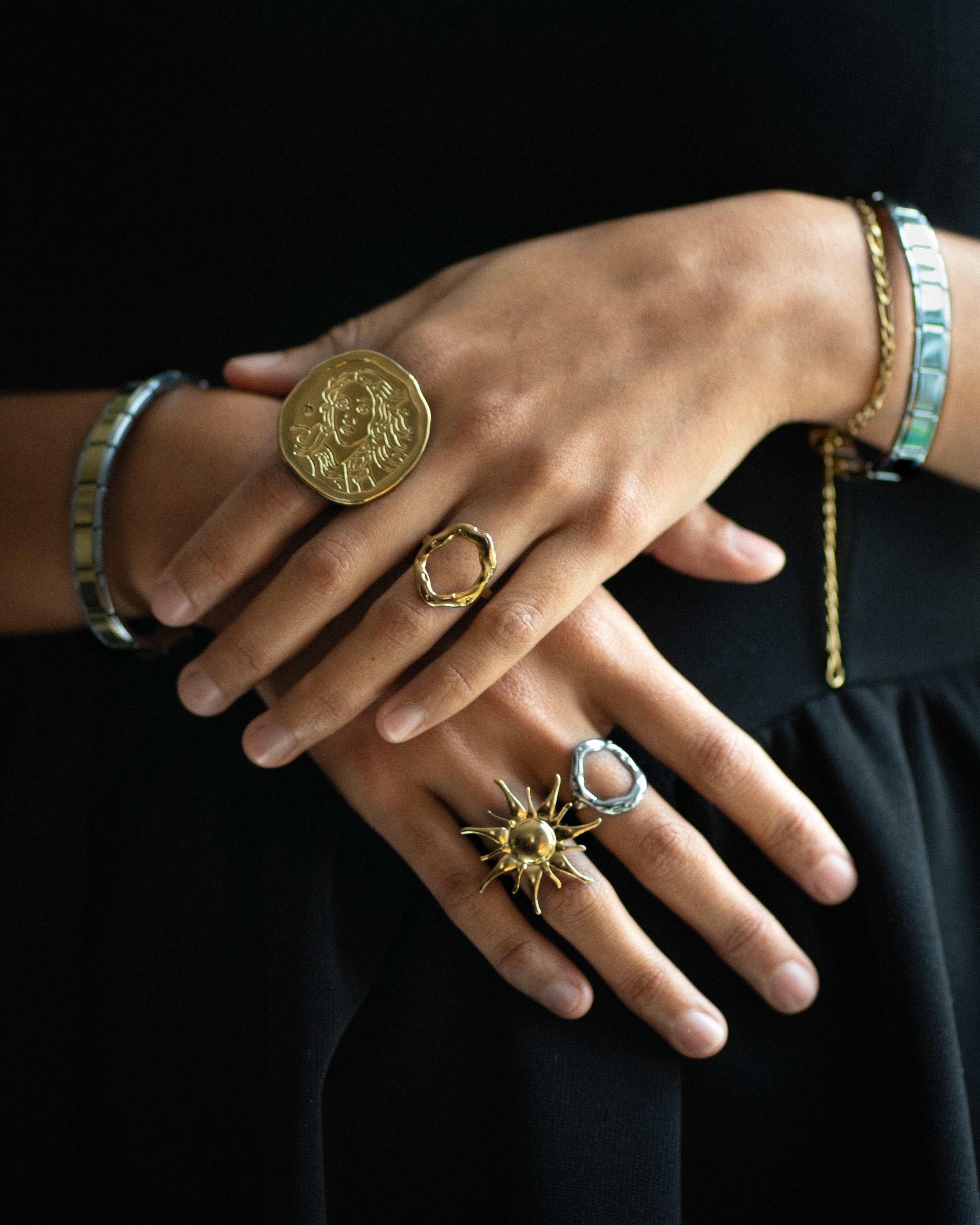 Manos con varios anillos y pulseras de oro y plata, negro de fondo.