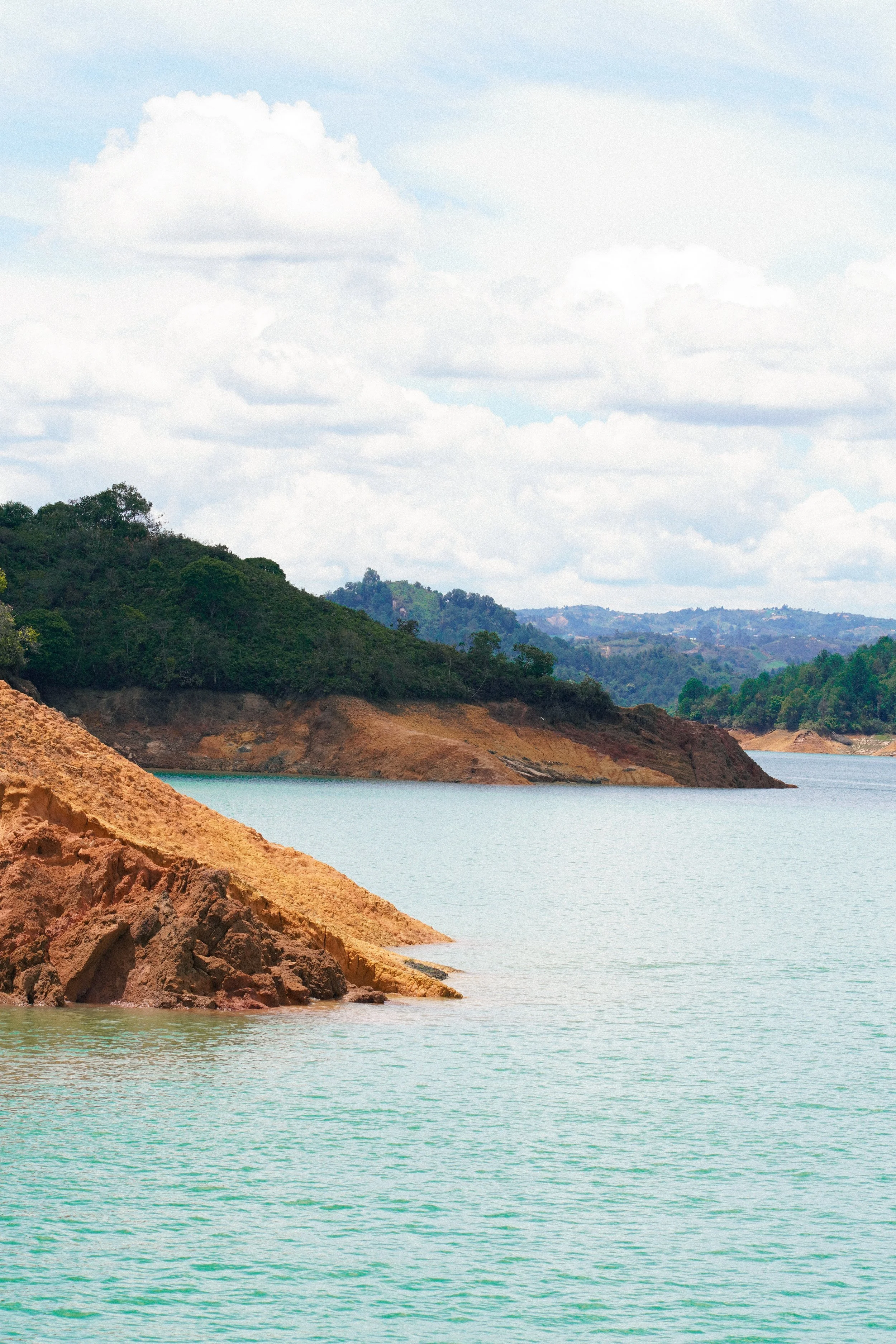Imagen de un paisaje con agua, colinas y árboles bajo un cielo con nubes.