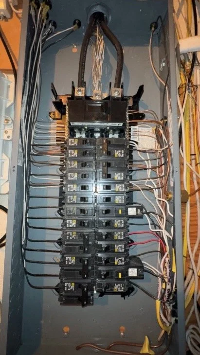 Electrical panel with circuit breakers and wiring inside a gray electrical box.