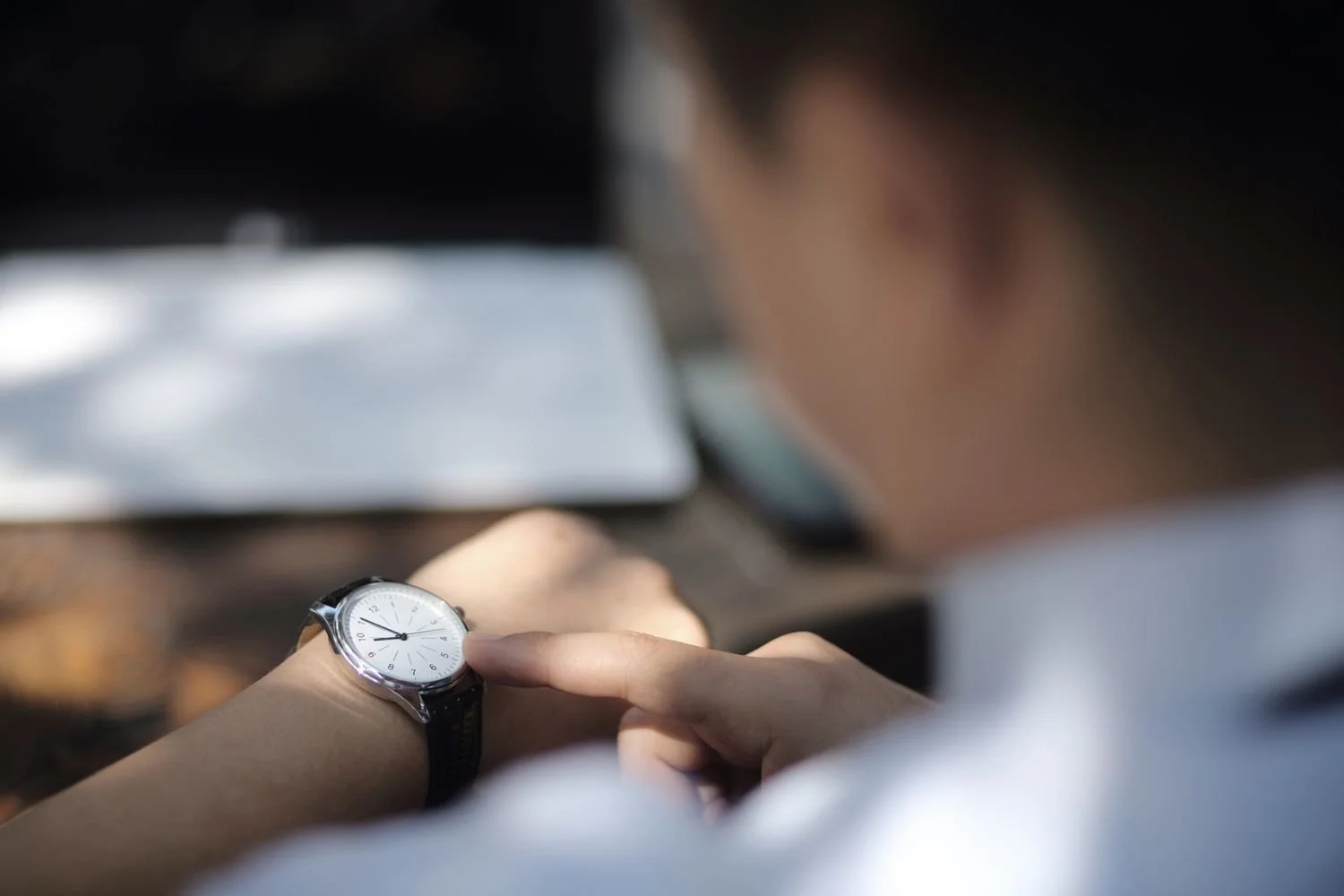 Person looking at a watch on their wrist, with focus on the watch and a blurred background.