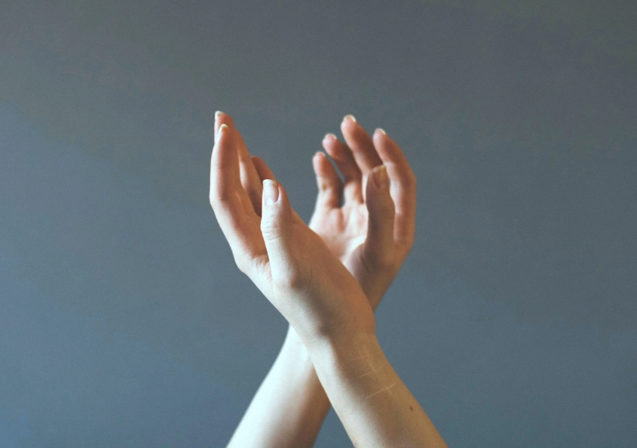 Two hands with interlocked fingers raised against a dark background.