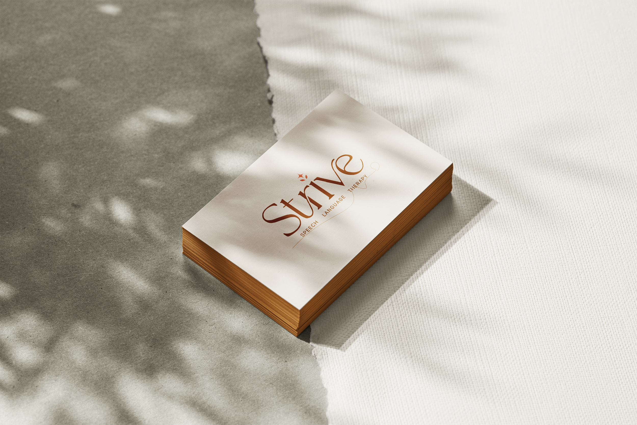 A stack of business cards for 'Strive' speech, language therapy on a textured surface with light shadows.