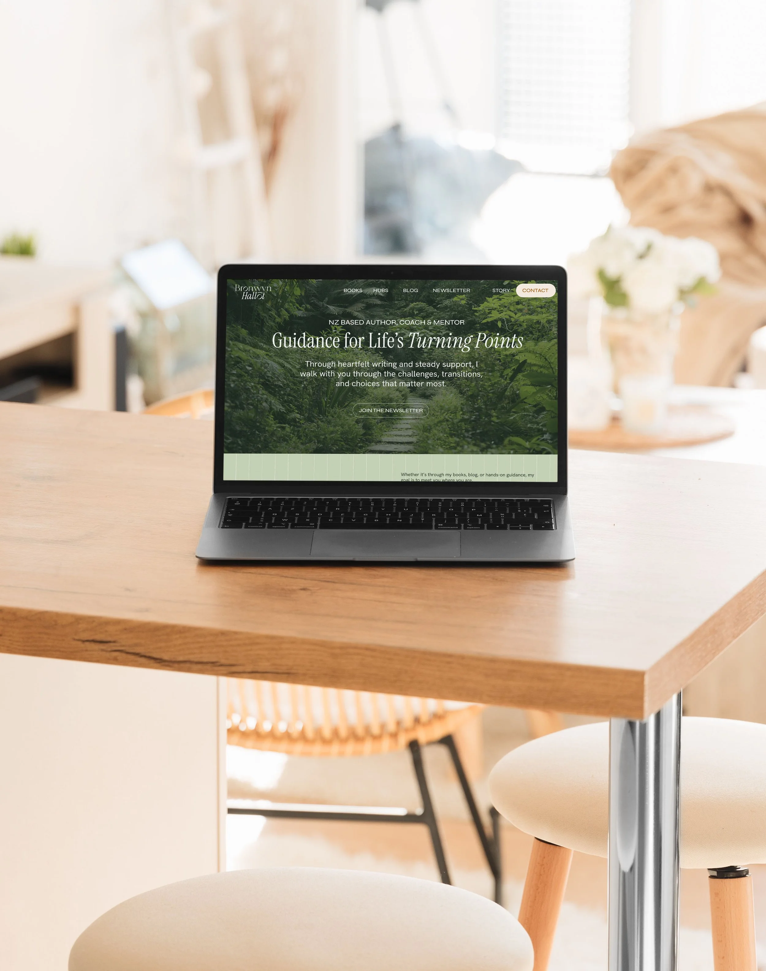 Open laptop on a wooden table displaying a website for a life coach called Bronwyn Hallot, with a green forest background and navigation menu.