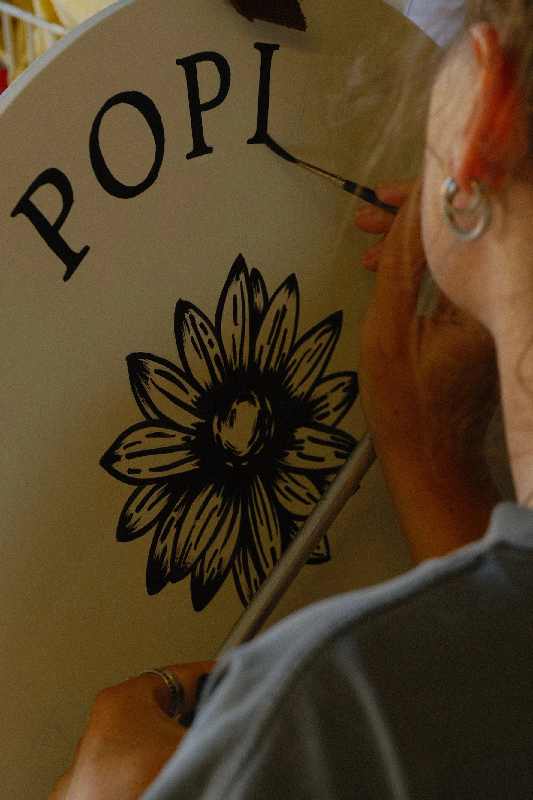 woman hand painting a black & white circular sign with a flower in the centre.