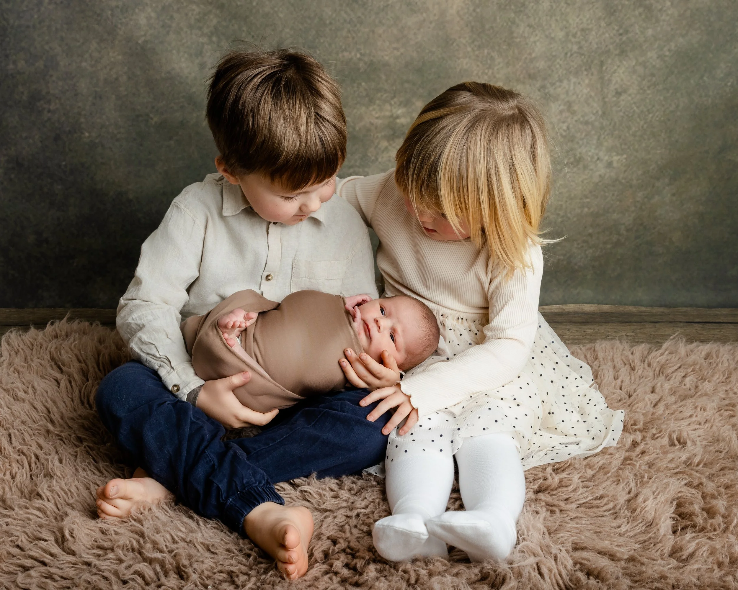 nyfødtfoto-søsken holder baby-brun bakgrunn-bergen.jpeg