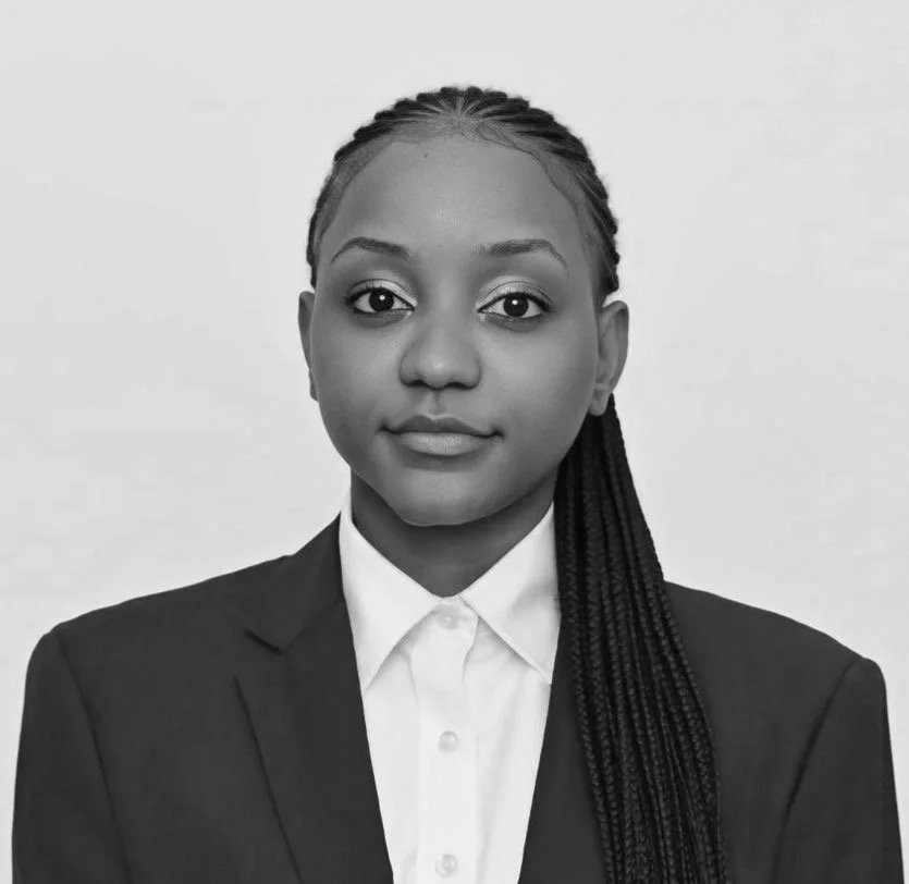 Black and white professional portrait of young woman with braided hair wearing a suit jacket and collared shirt.